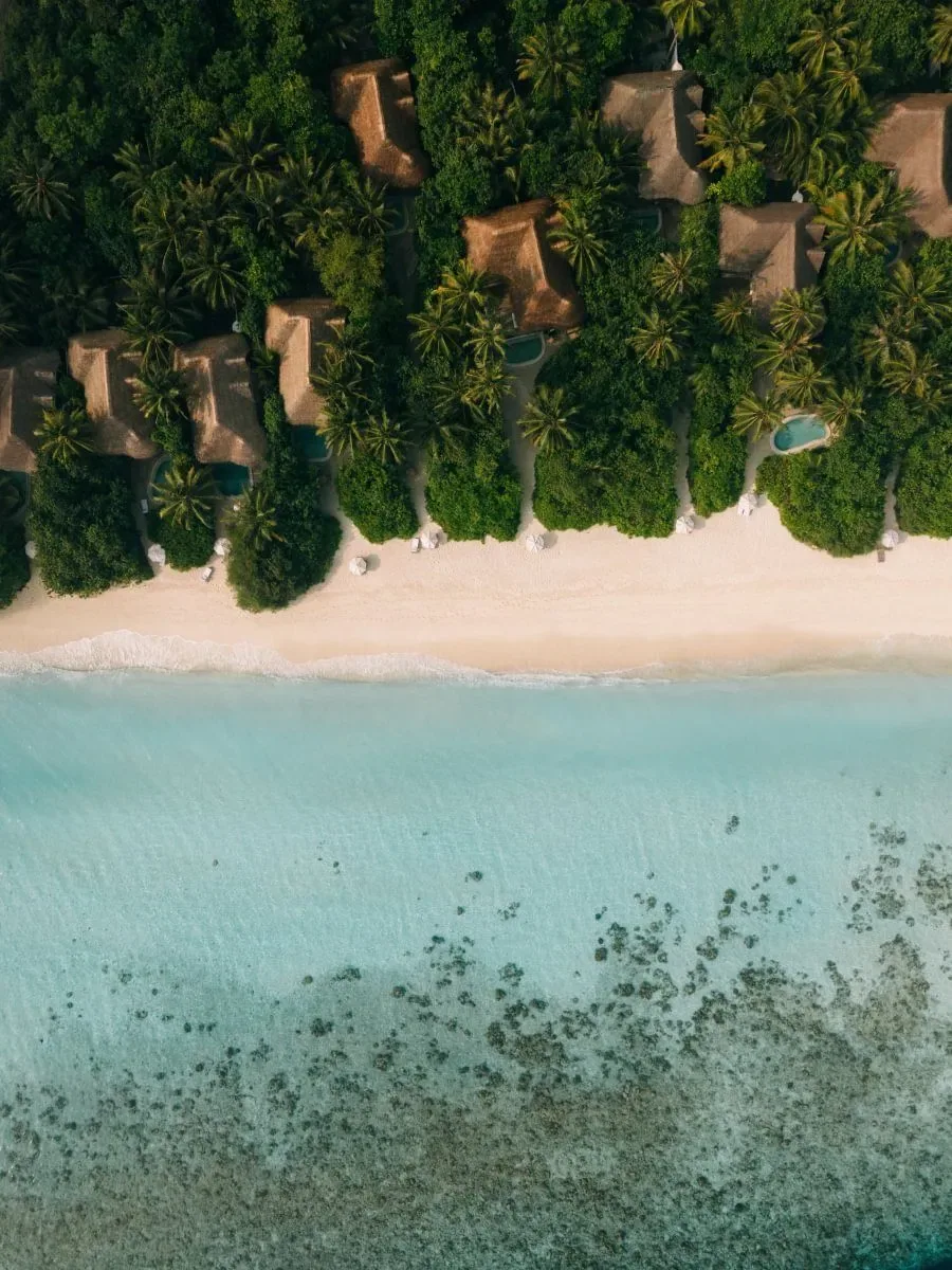 Luftaufnahme des Strands von Soneva Fushi mit Palmen und flachem türkisfarbenem Wasser