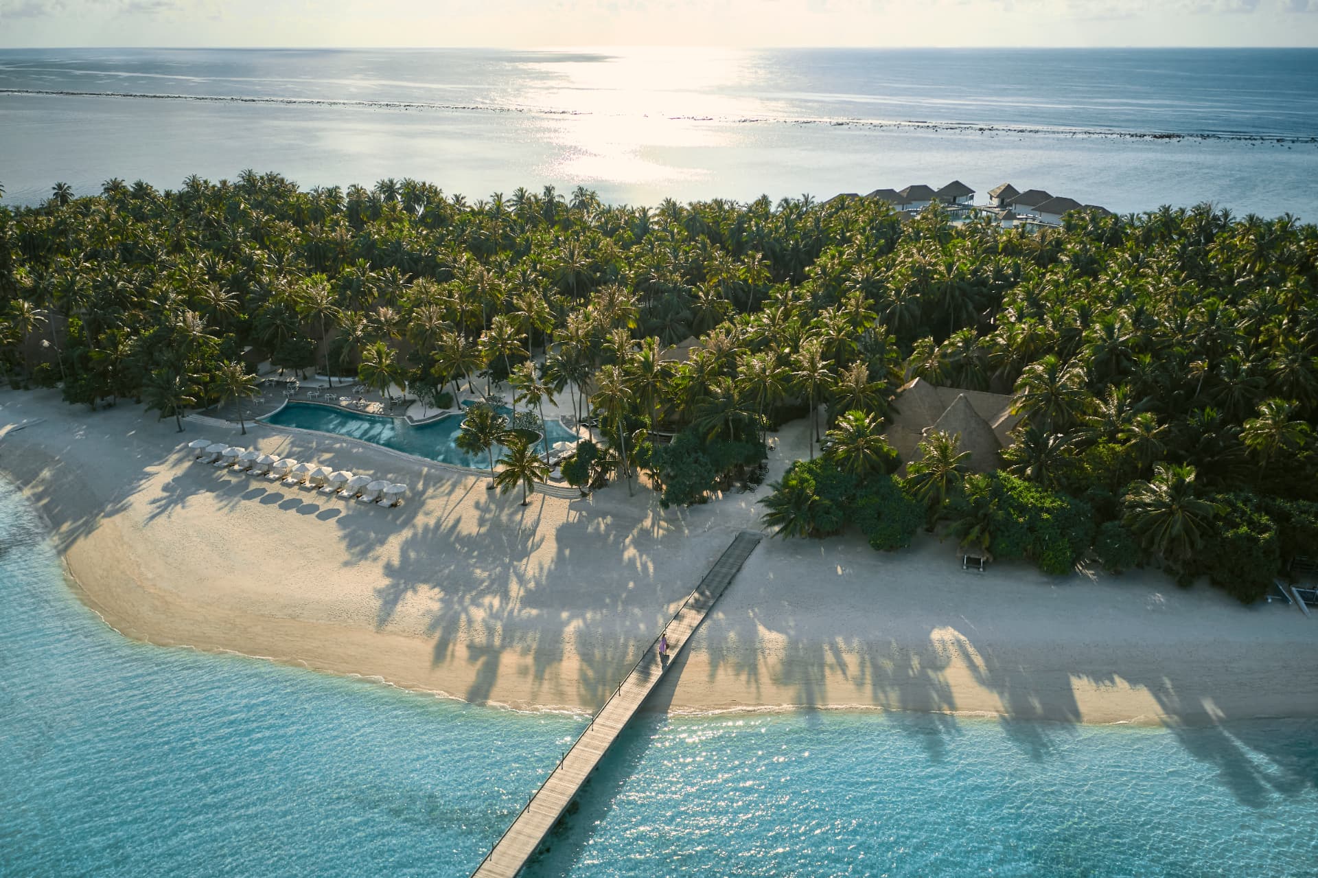 Die Insel aus der Luft: Pool, Strand und Steg vor dichtem Palmenwald