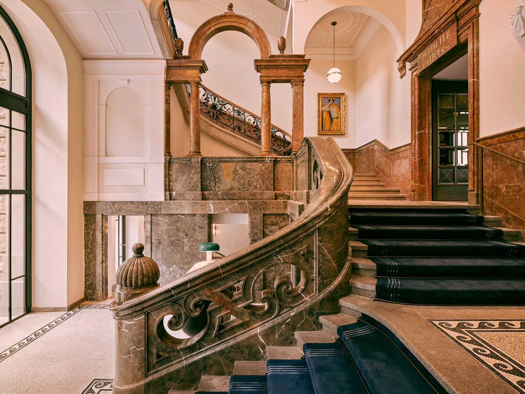 Historisches Treppenhaus im Rosewood Munich mit Marmorgeländer, Mosaikboden und dunkelblauem Läufer