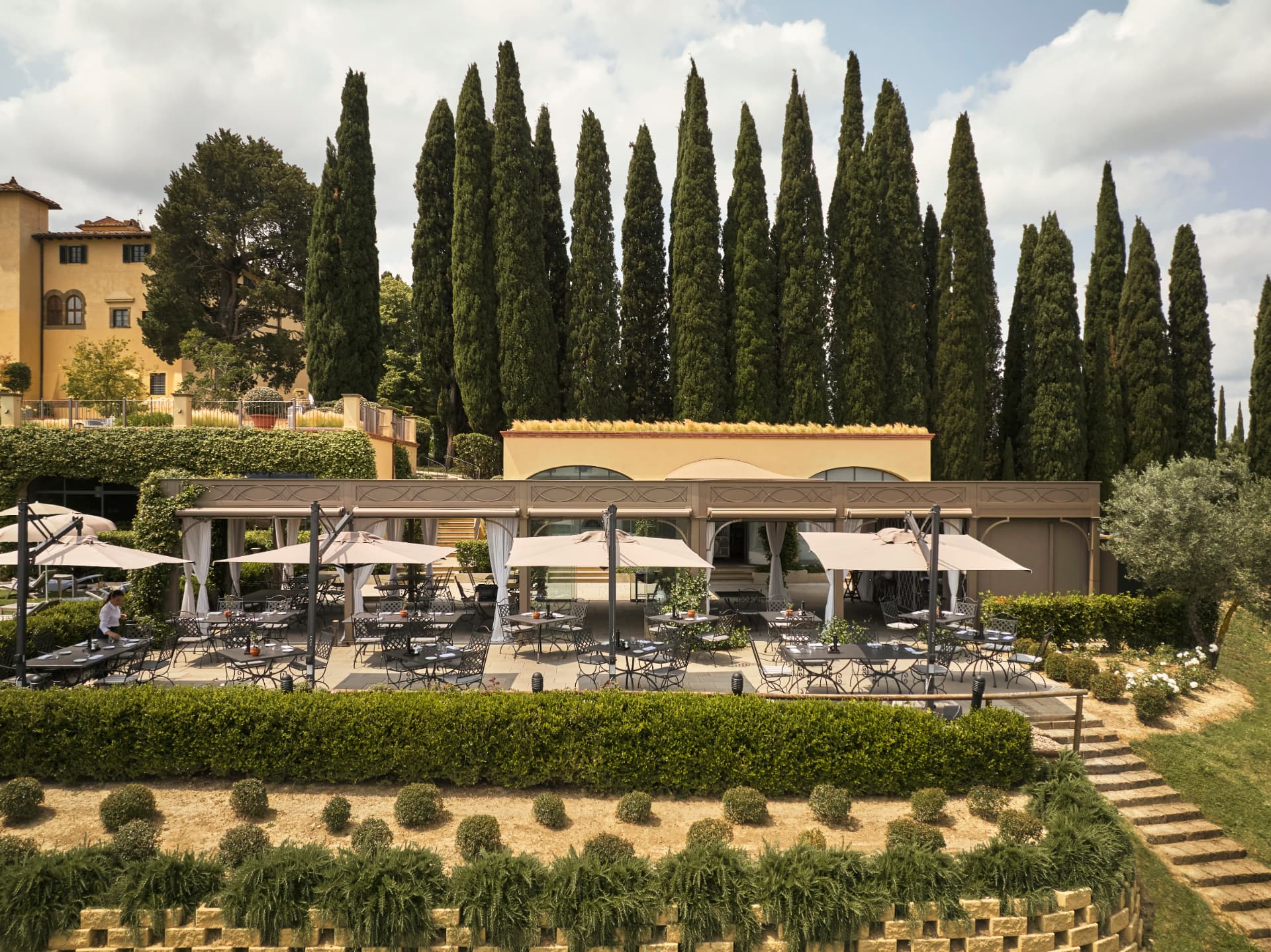 Pavillion-Restaurant vor dem gelben Castello, gerahmt von Zypressen im Chianti