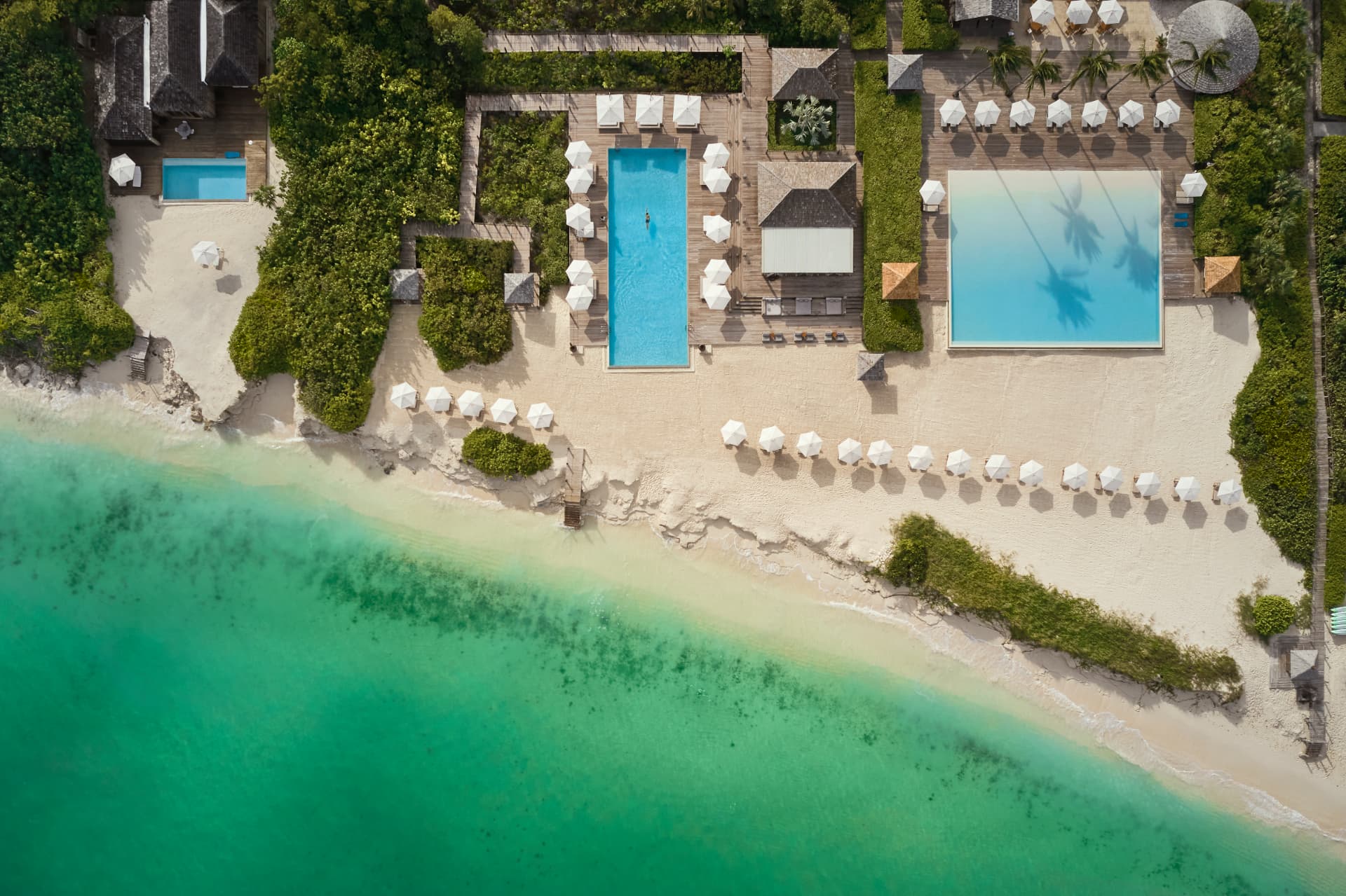Senkrechte Luftaufnahme der beiden Pools zwischen Sand, Grün und türkisem Wasser