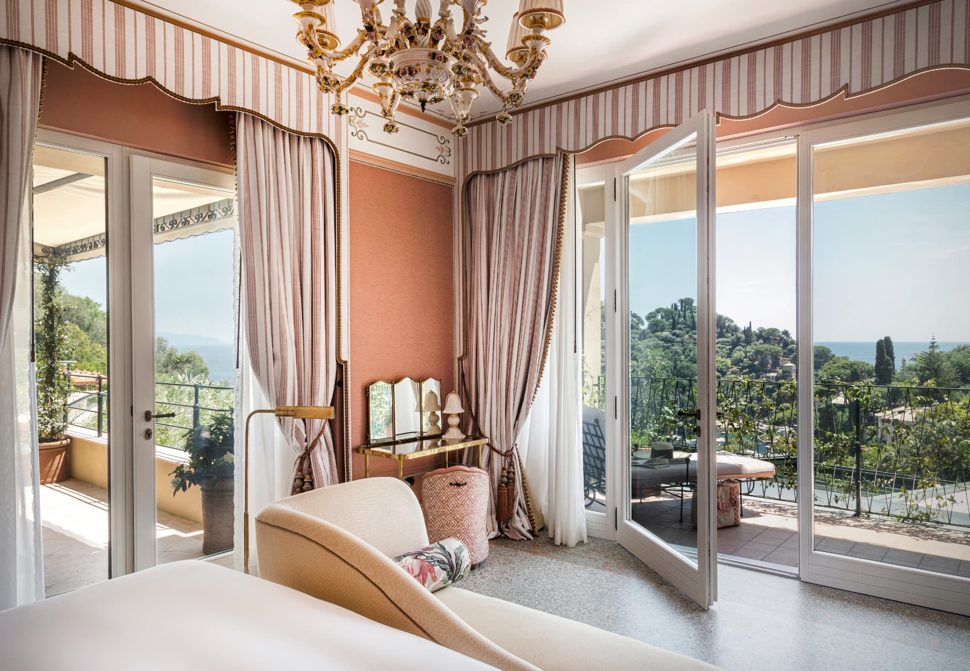 Suite mit geöffneten Flügeltüren zur Terrasse, gestreiften Vorhängen und Blick über Pinien aufs Meer