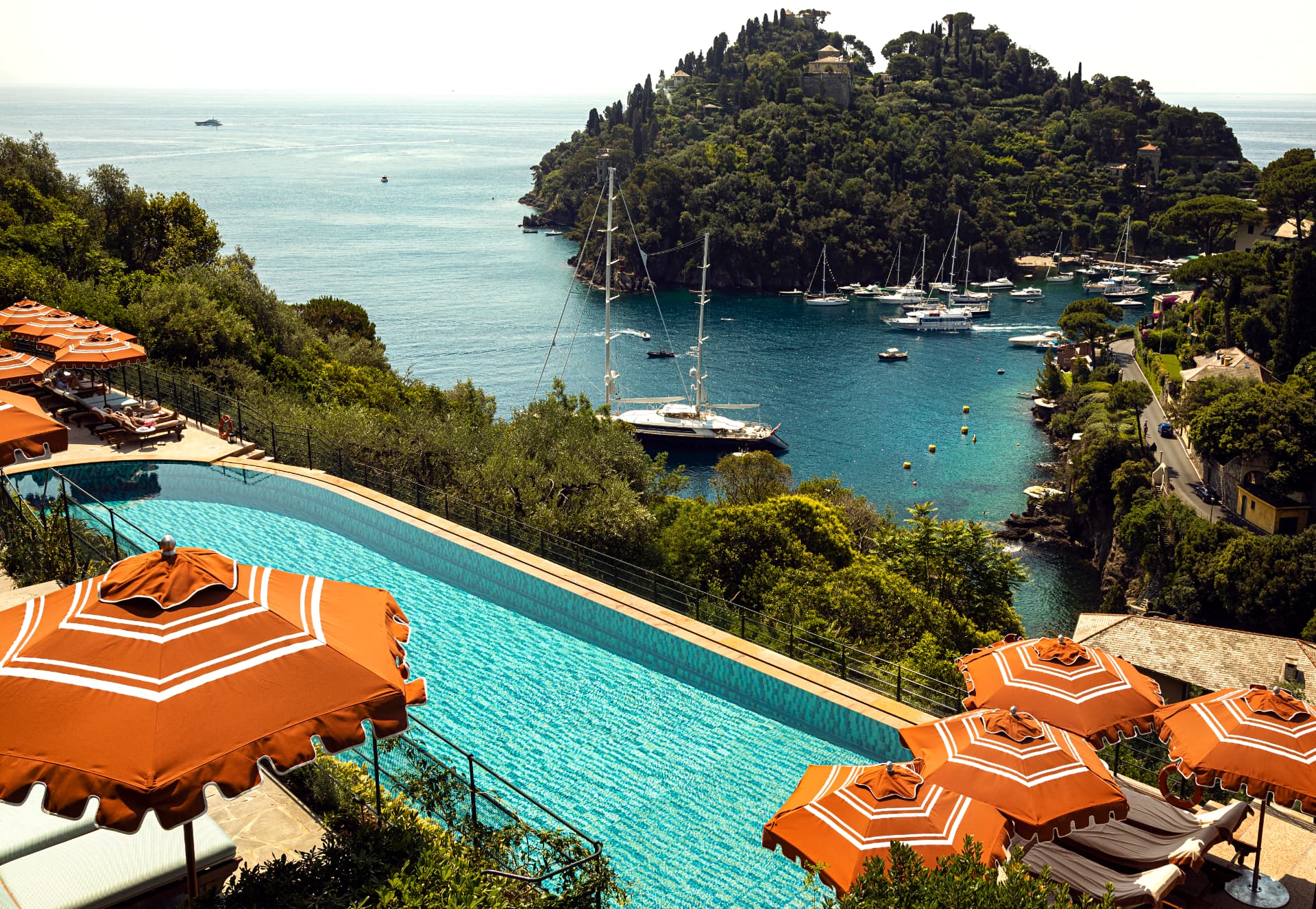Der Pool des Splendido über der Bucht von Portofino, davor orangefarbene Schirme, dahinter Segelyachten im Hafen