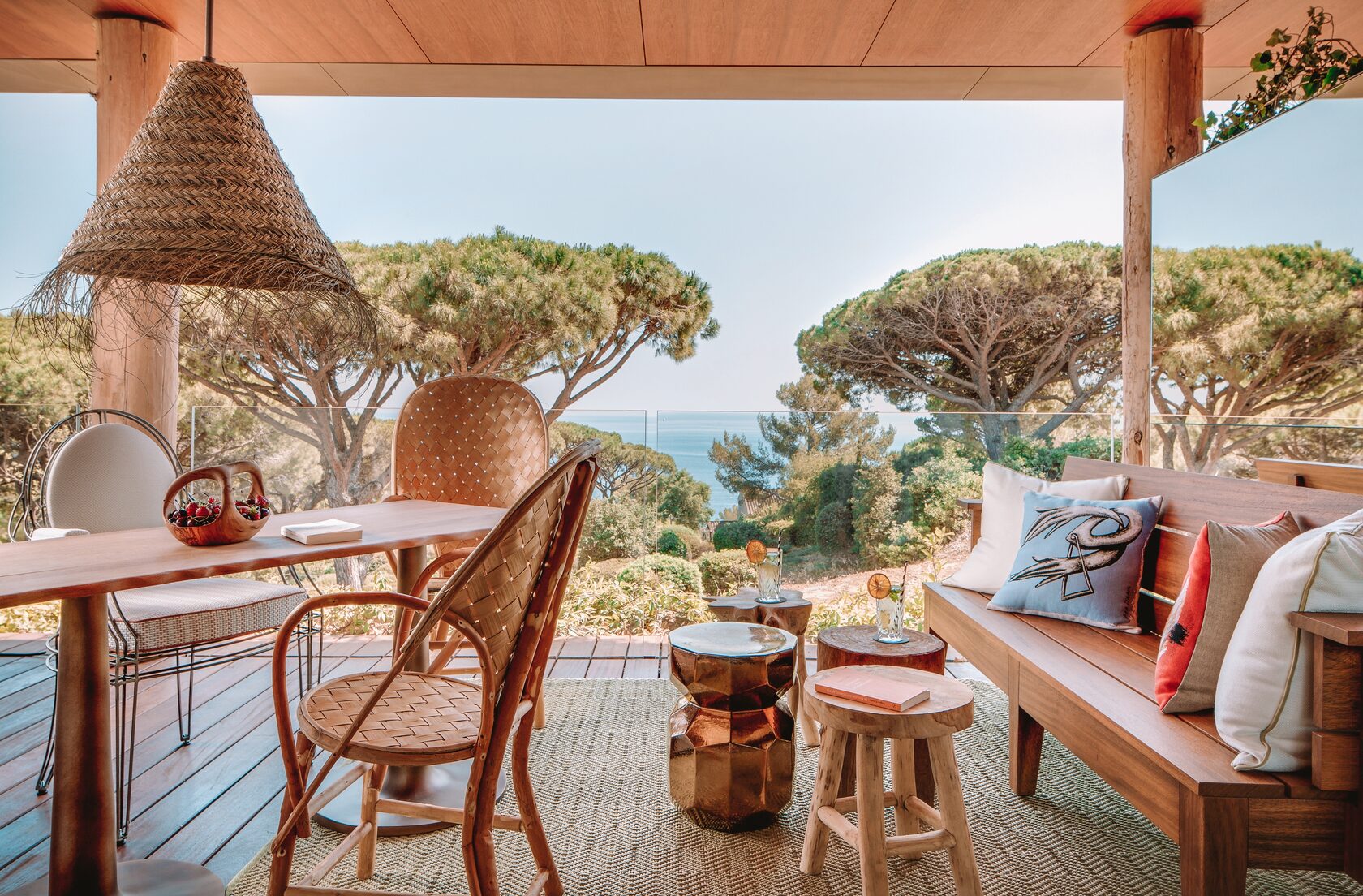 Terrasse aus Holz mit Korbmöbeln, Pinien und Blick auf das Mittelmeer