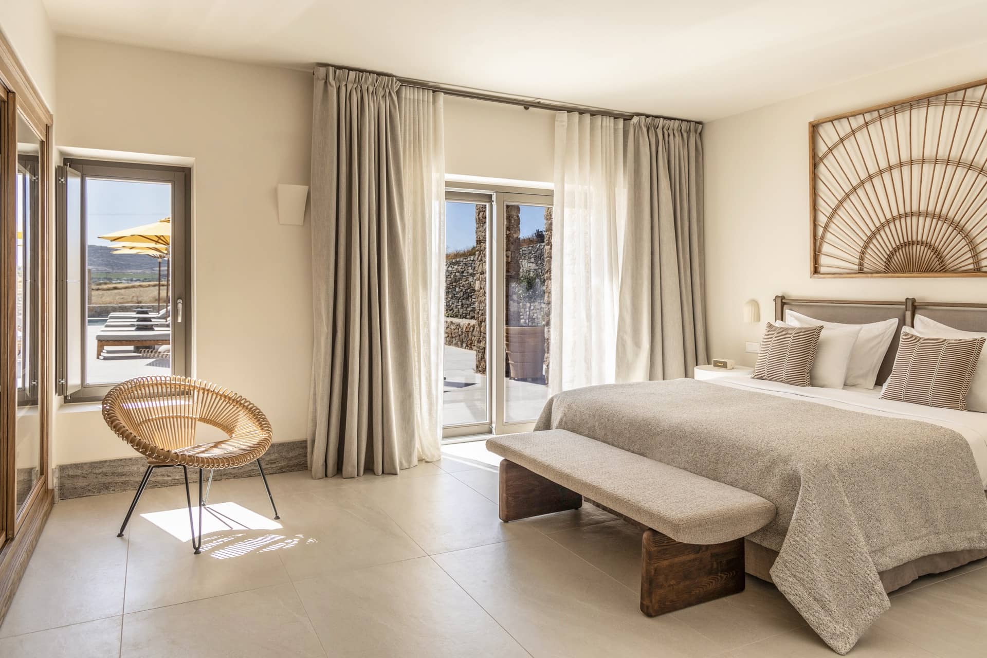Schlafzimmer einer Villa im Parīlio mit Leinenvorhängen, Rattansessel und Fächerarbeit über dem Bett