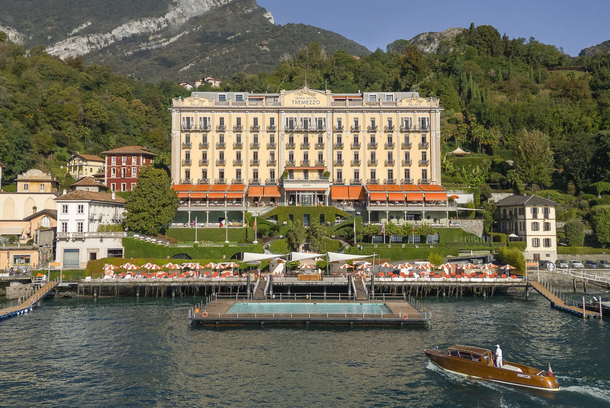 Fassade des Grand Hotel Tremezzo vom Wasser aus, davor der schwimmende Pool und ein Holzboot