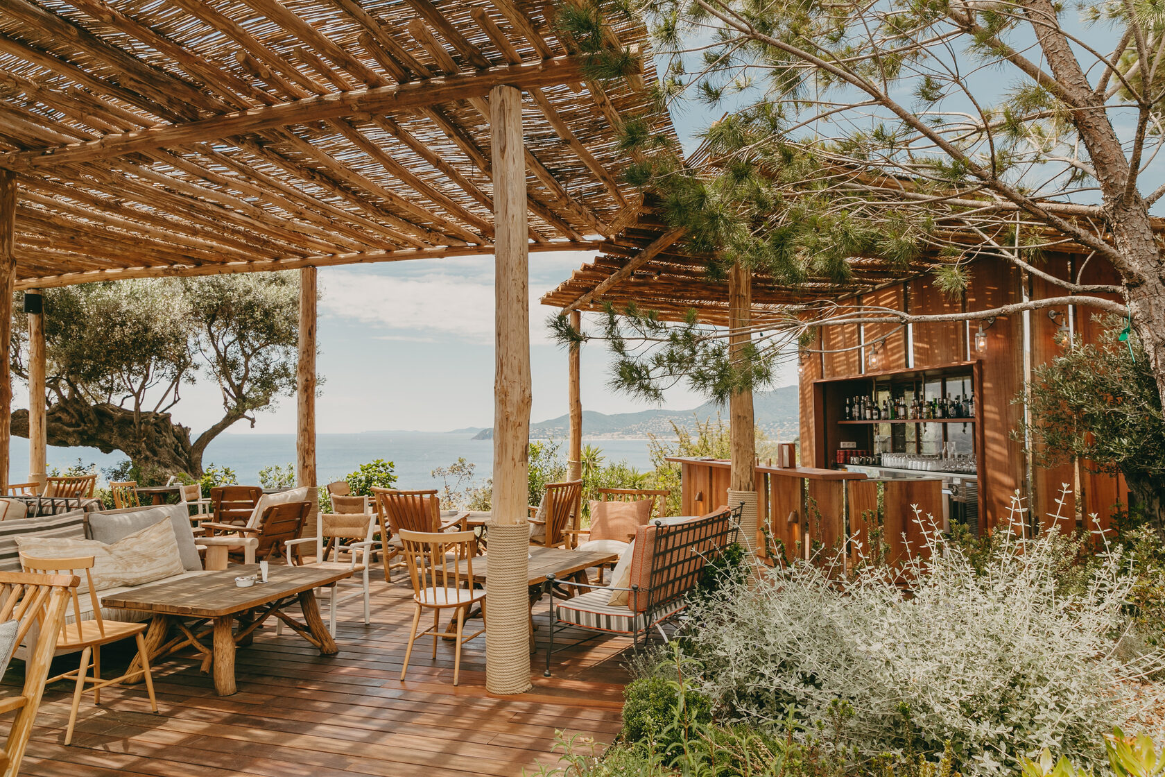 Bar unter der Schilfpergola mit Holzmöbeln, Olivenbäumen und Blick auf die Bucht