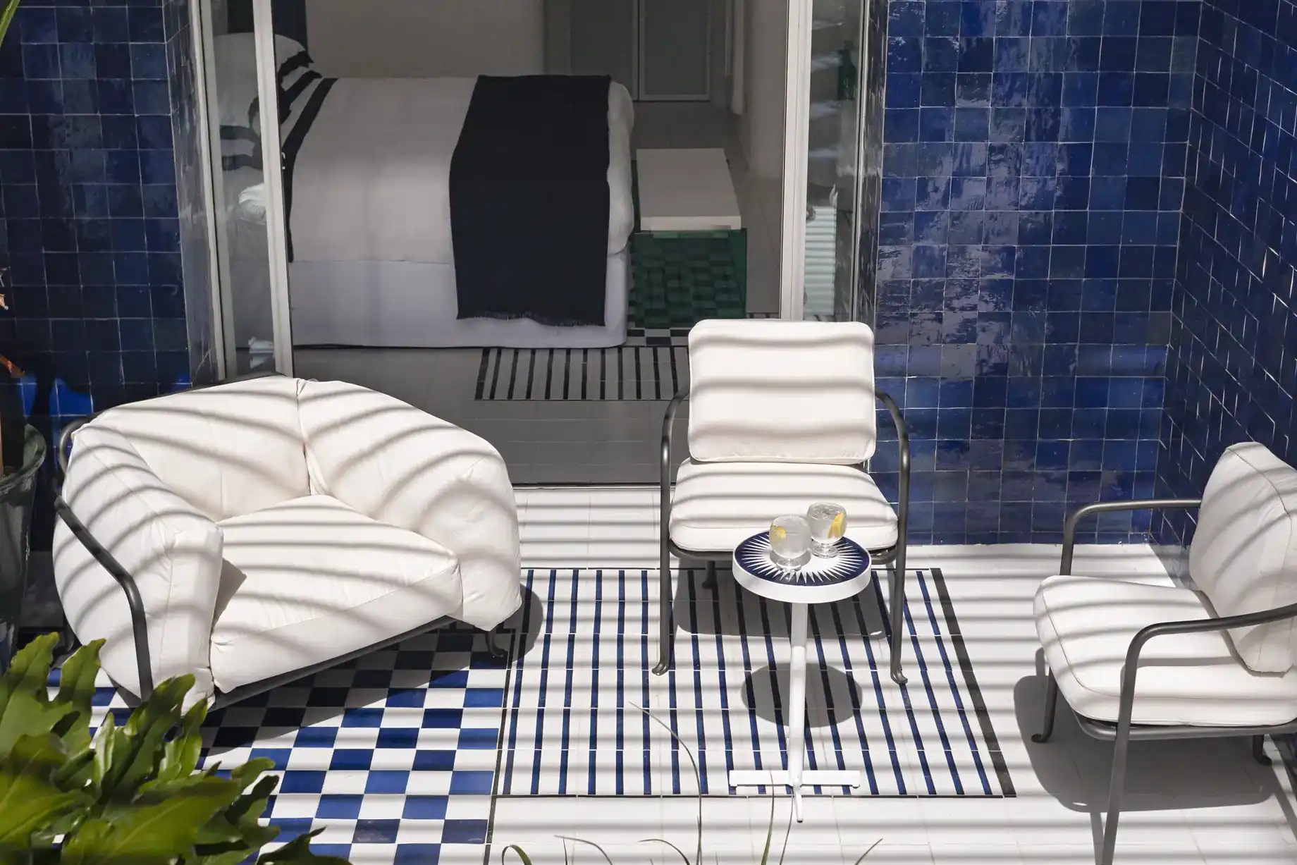 Zimmerterrasse mit blau glasierten Fliesen, weißen Sesseln und Blick ins Schlafzimmer