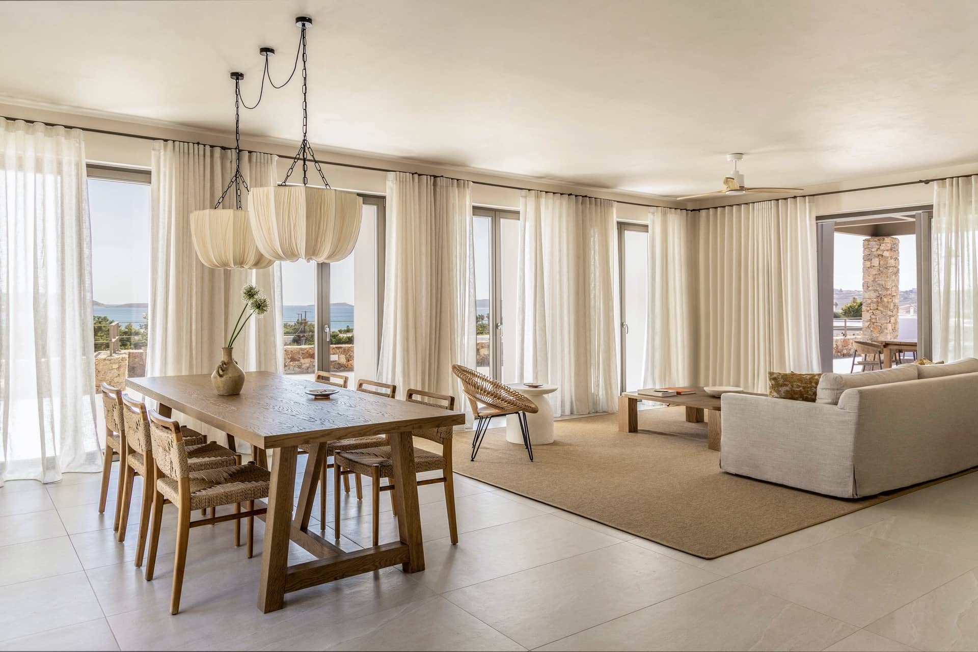 Wohn- und Essbereich einer Villa im Parīlio mit langem Eichentisch, Leinenlampen und Blick auf die Bucht
