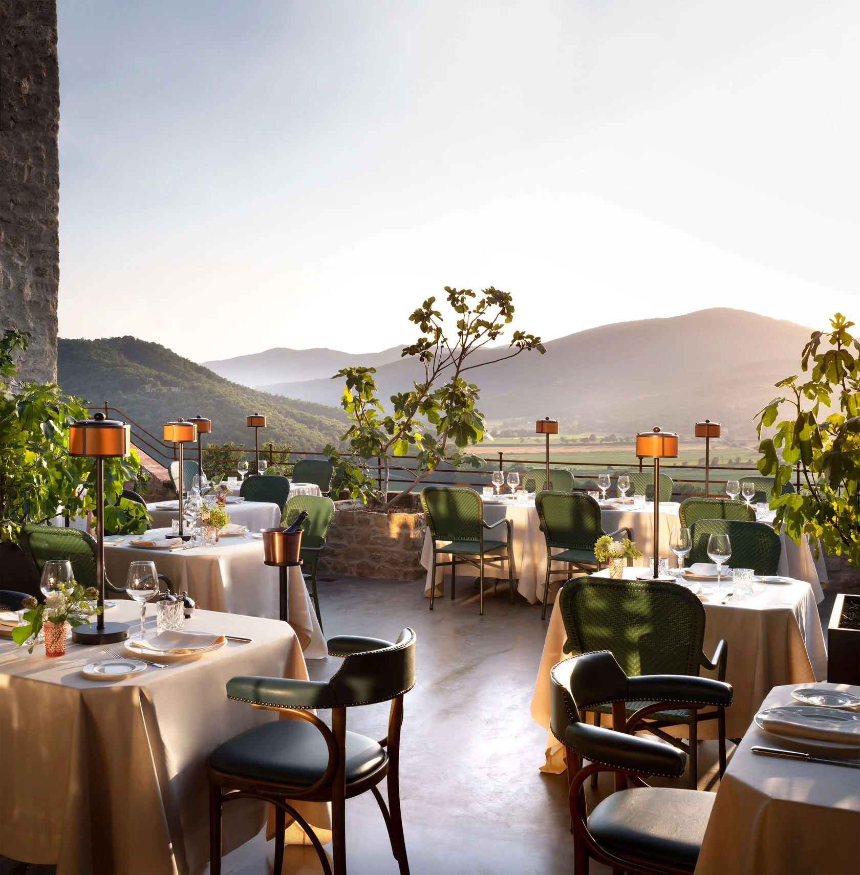Terrasse mit gedeckten Tischen, grünen Stühlen und Blick über die Hügel im Abendlicht