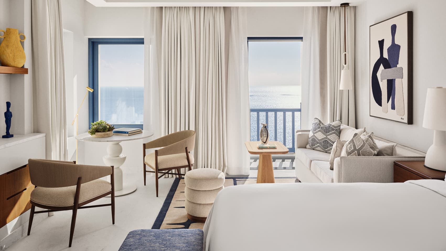 Helles Zimmer mit blau gefassten Fenstern, Sitzgruppe und Blick auf das Meer