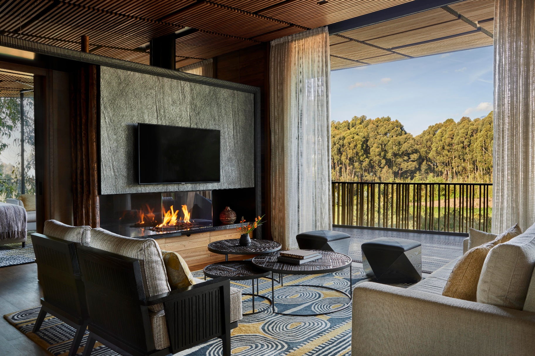 Private Holzterrasse einer ruandischen Waldlodge im Morgennebel mit zwei Holzstühlen, einer Wolldecke und einer handgefertigten Keramiktasse