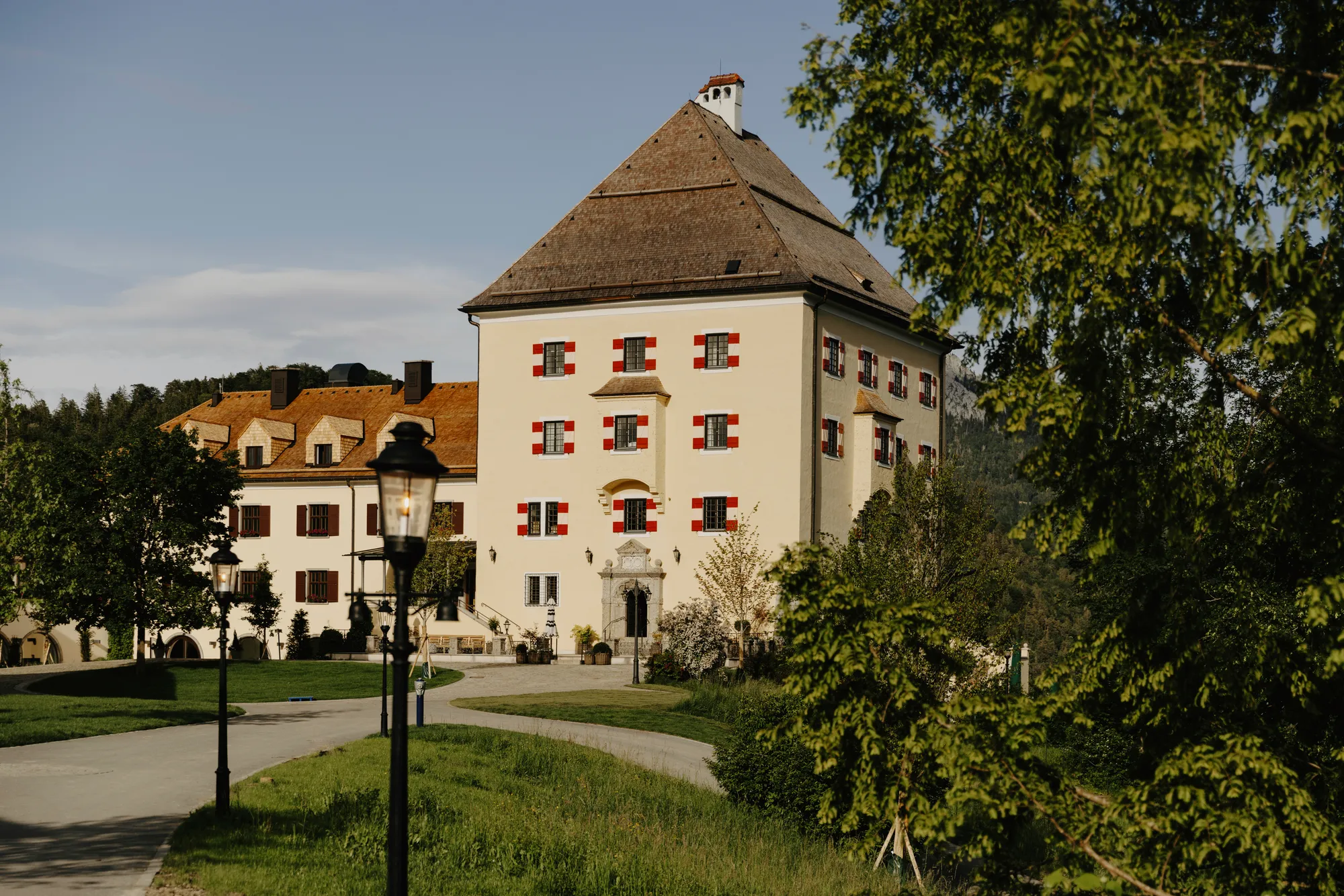 Fassade des Schloss Fuschl mit rot gerahmten Fenstern, Schindeldach und Zufahrt im Abendlicht