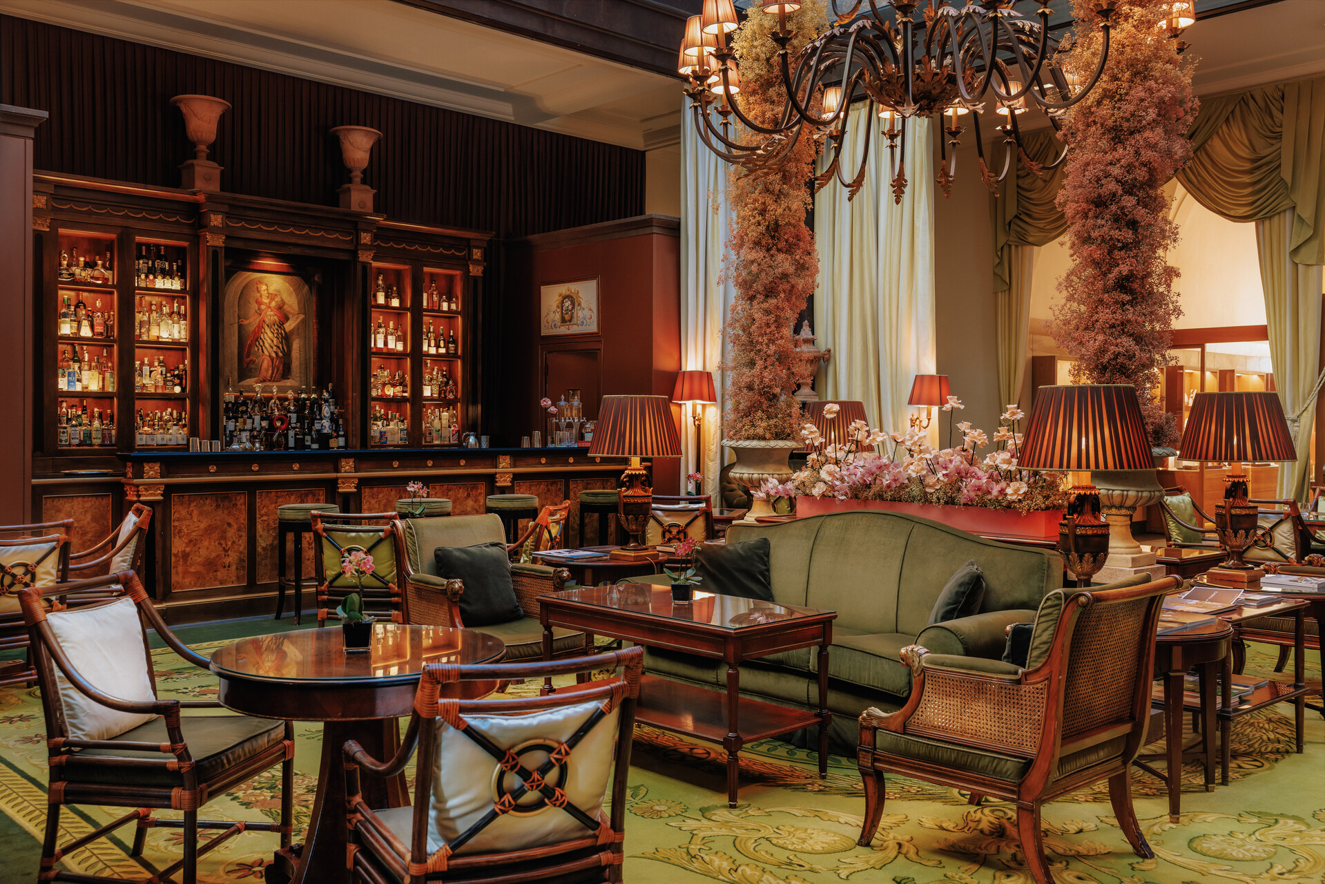Atrium-Bar mit grünen Samtsofas, dunklem Holz und Blumen unter dem Glasdach