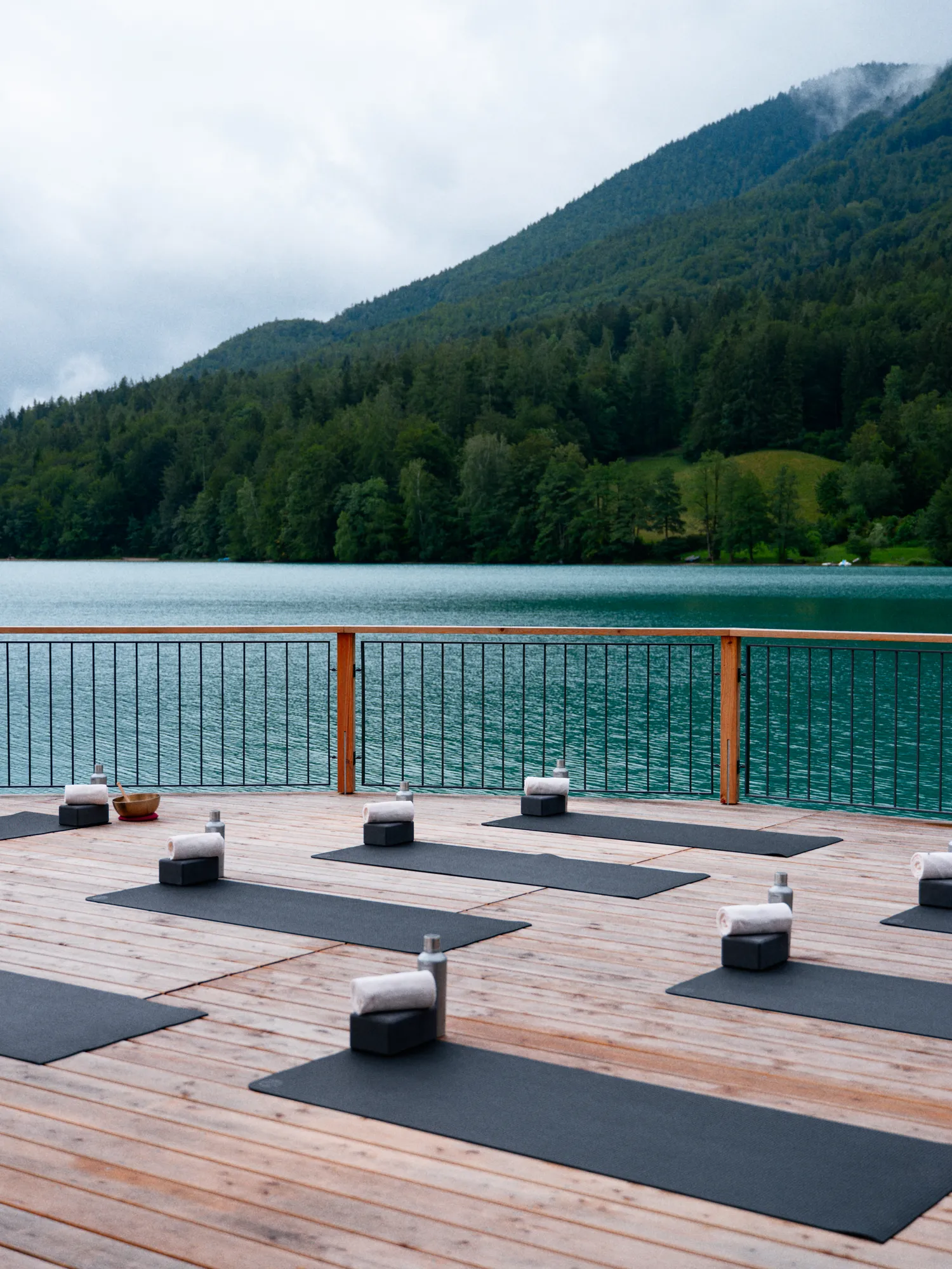 Yogadeck am Fuschlsee mit ausgelegten Matten, Klangschale und Blick auf den bewaldeten Hang gegenüber