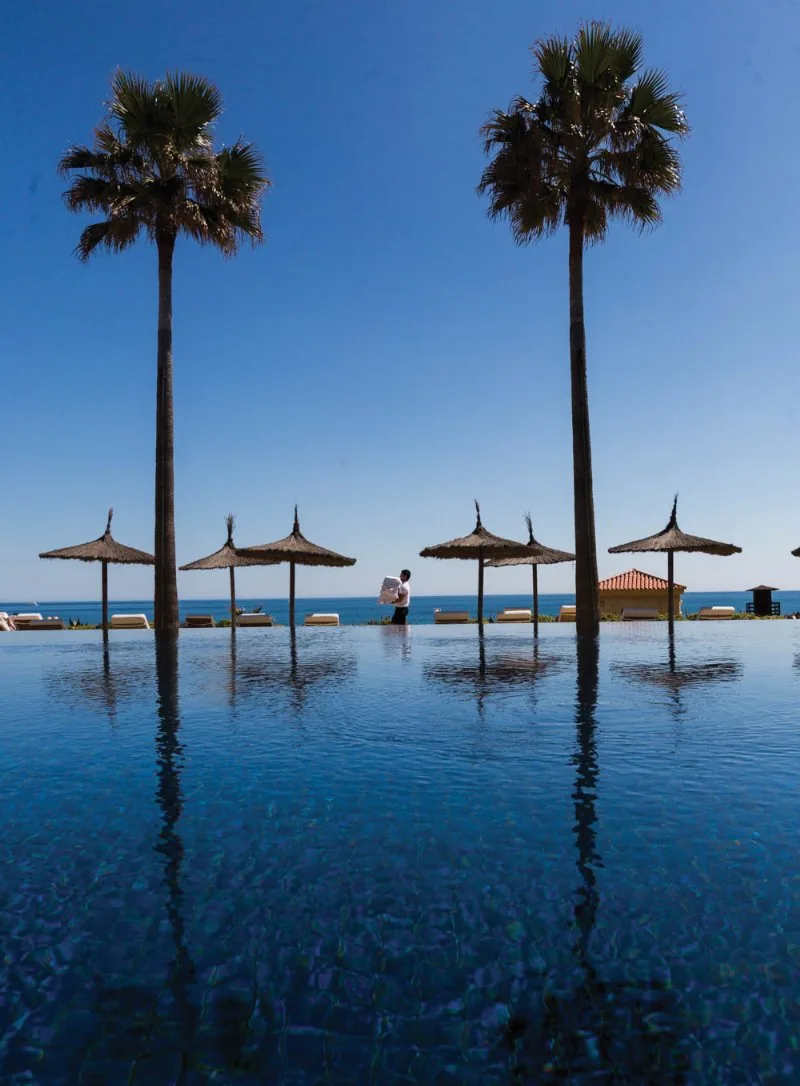 Pool der Finca Cortesin mit Palmen und Strohschirmen im Wasser