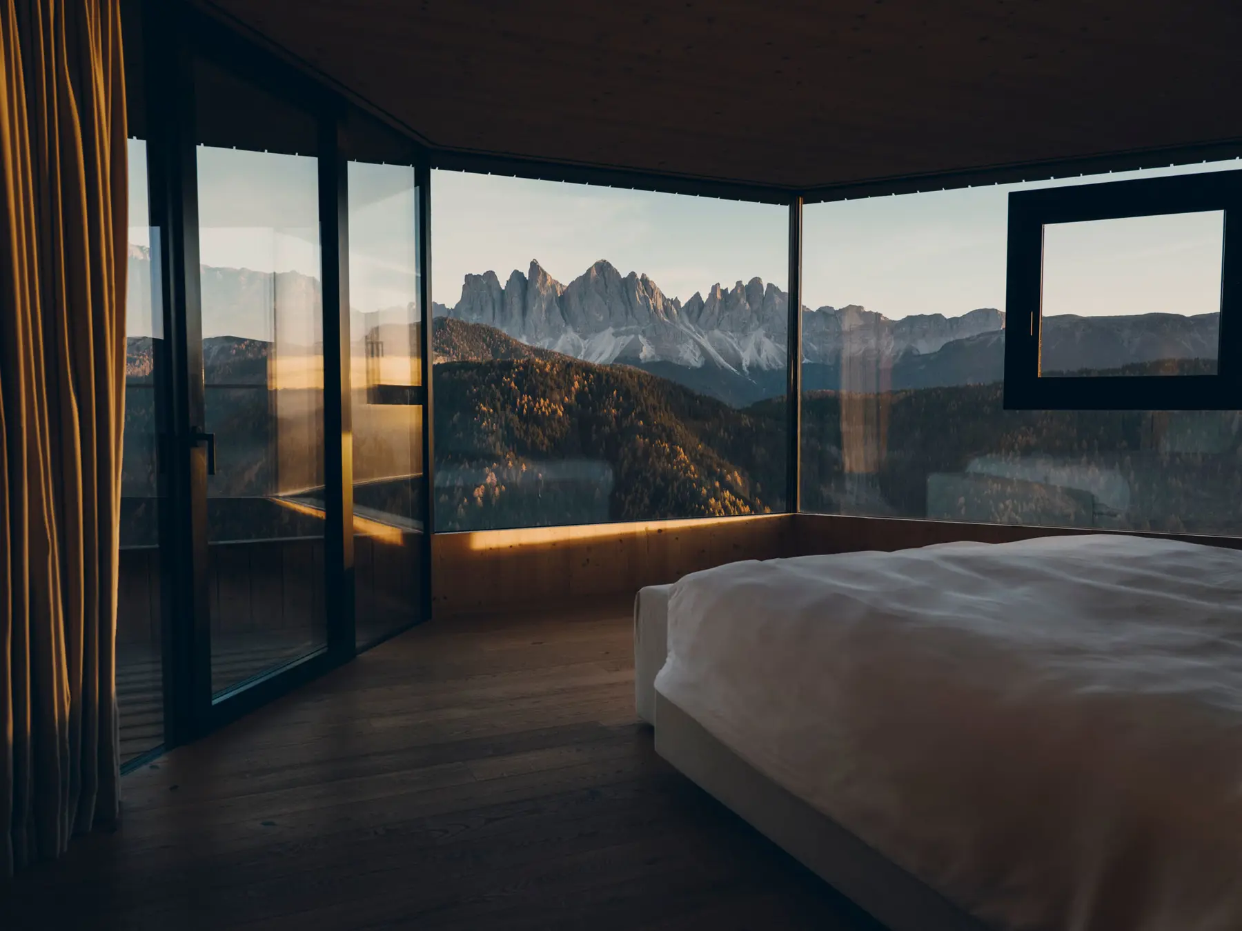 Zimmer mit Eckverglasung und Blick auf die Geisler-Spitzen im Abendlicht