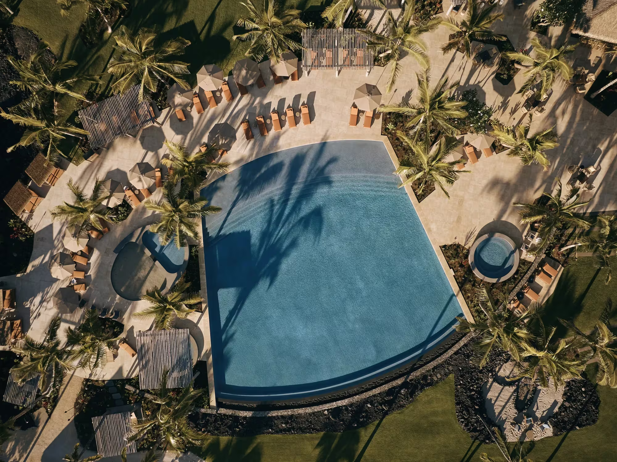 Luftaufnahme des Moana Pool im Rosewood Kona Village zwischen Palmen und Sand