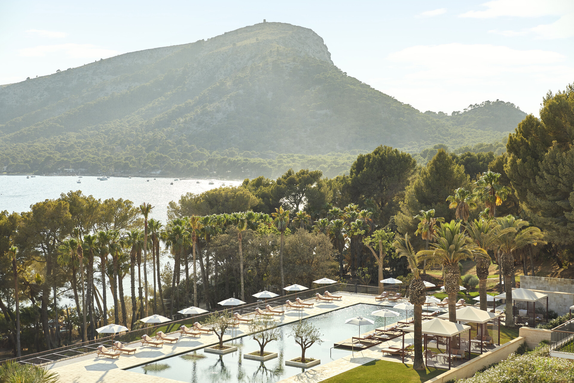 Blick über Pool, Pinien und Palmen der Anlage auf die Bucht von Formentor und den Bergrücken dahinter
