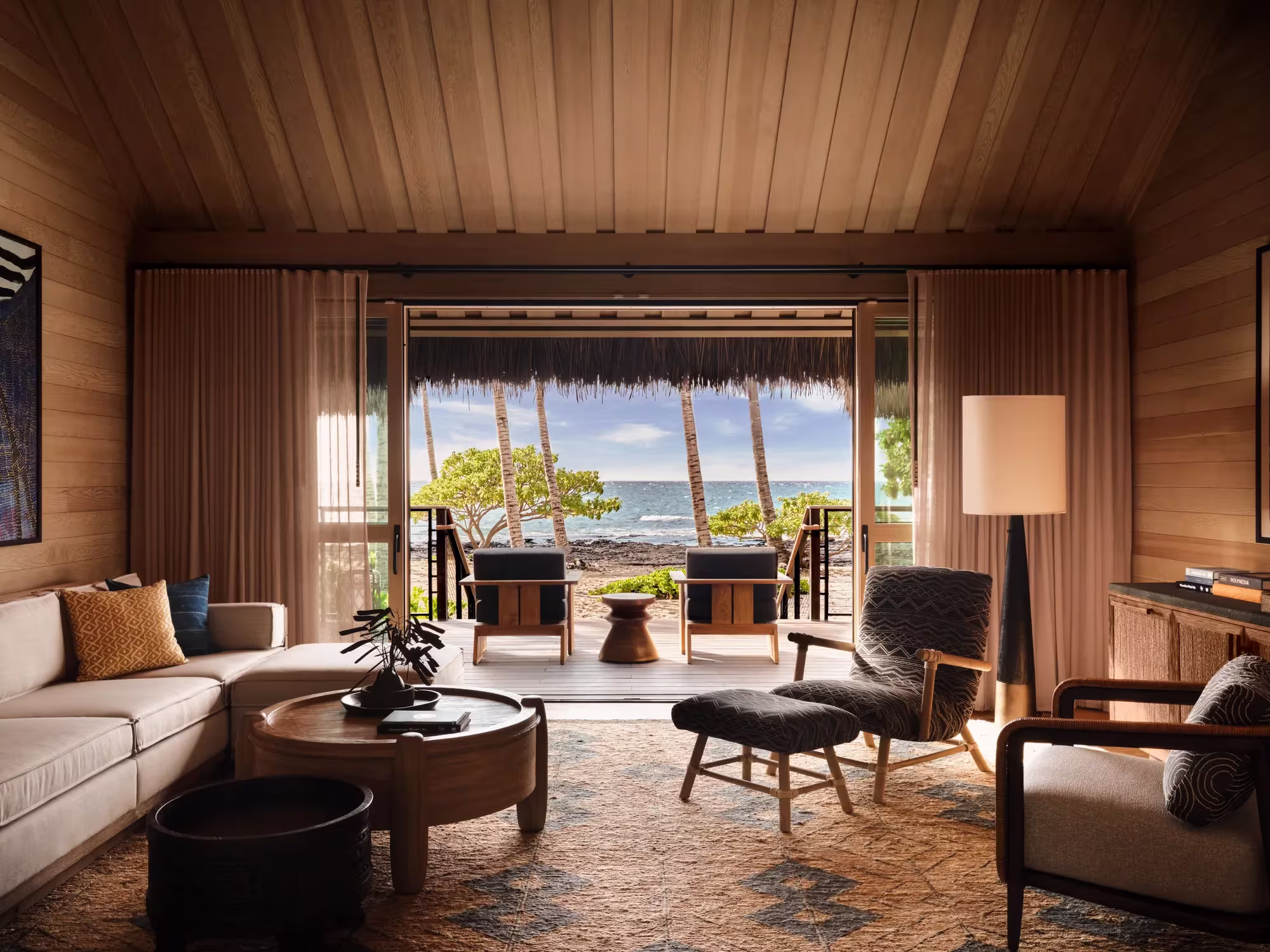Wohnbereich eines Beachfront Hale im Rosewood Kona Village mit offenen Türen zum Sand und hellem Holzinterieur