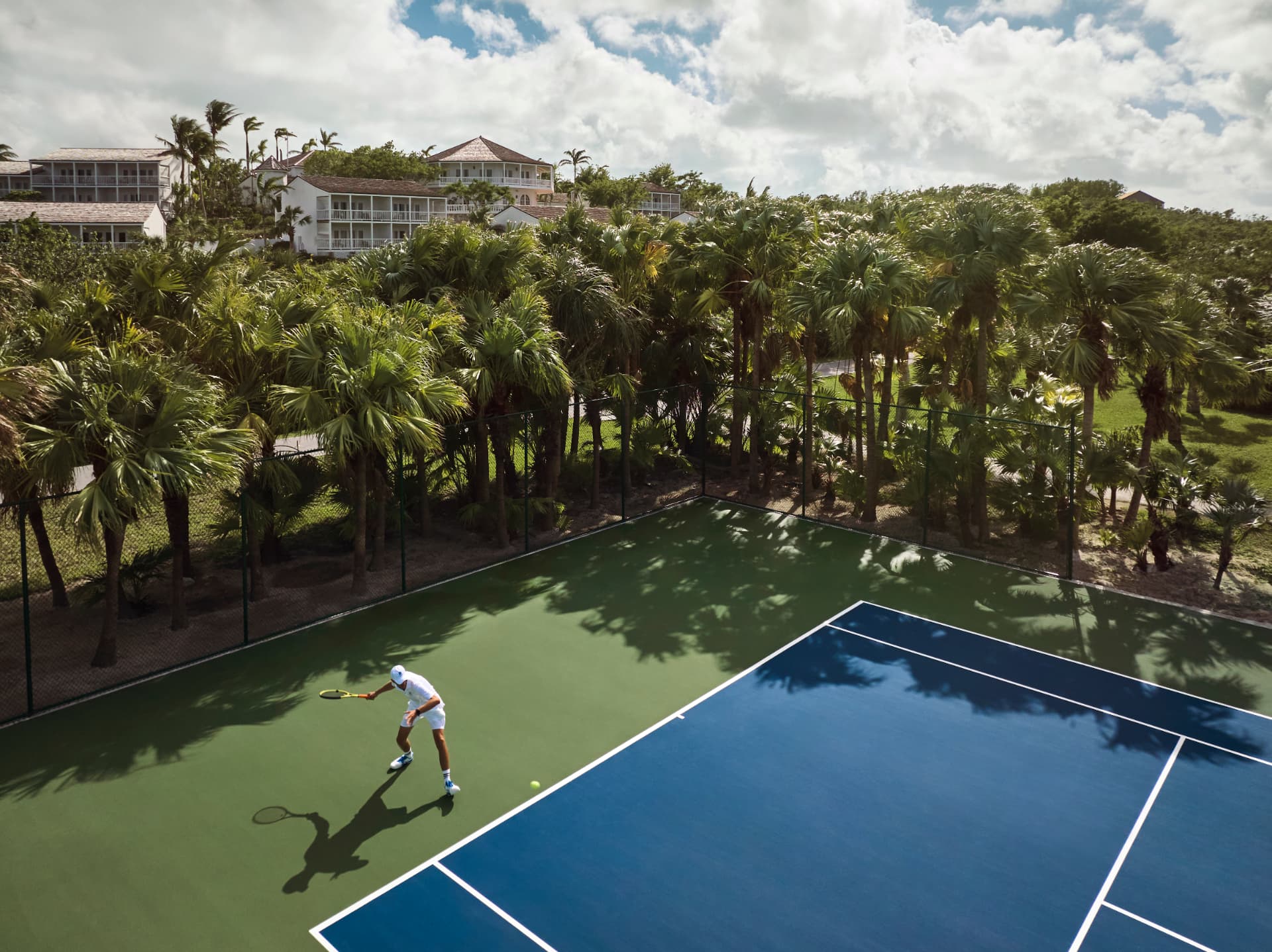 Tennisplatz zwischen Palmen, dahinter die weißen Häuser der Anlage