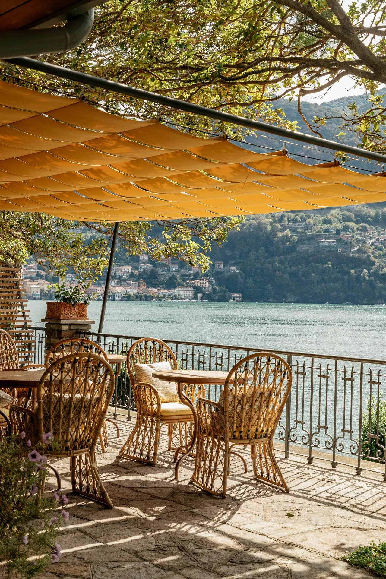 Terrasse des Passalacqua unter alten Bäumen mit Korbstühlen über dem Comer See