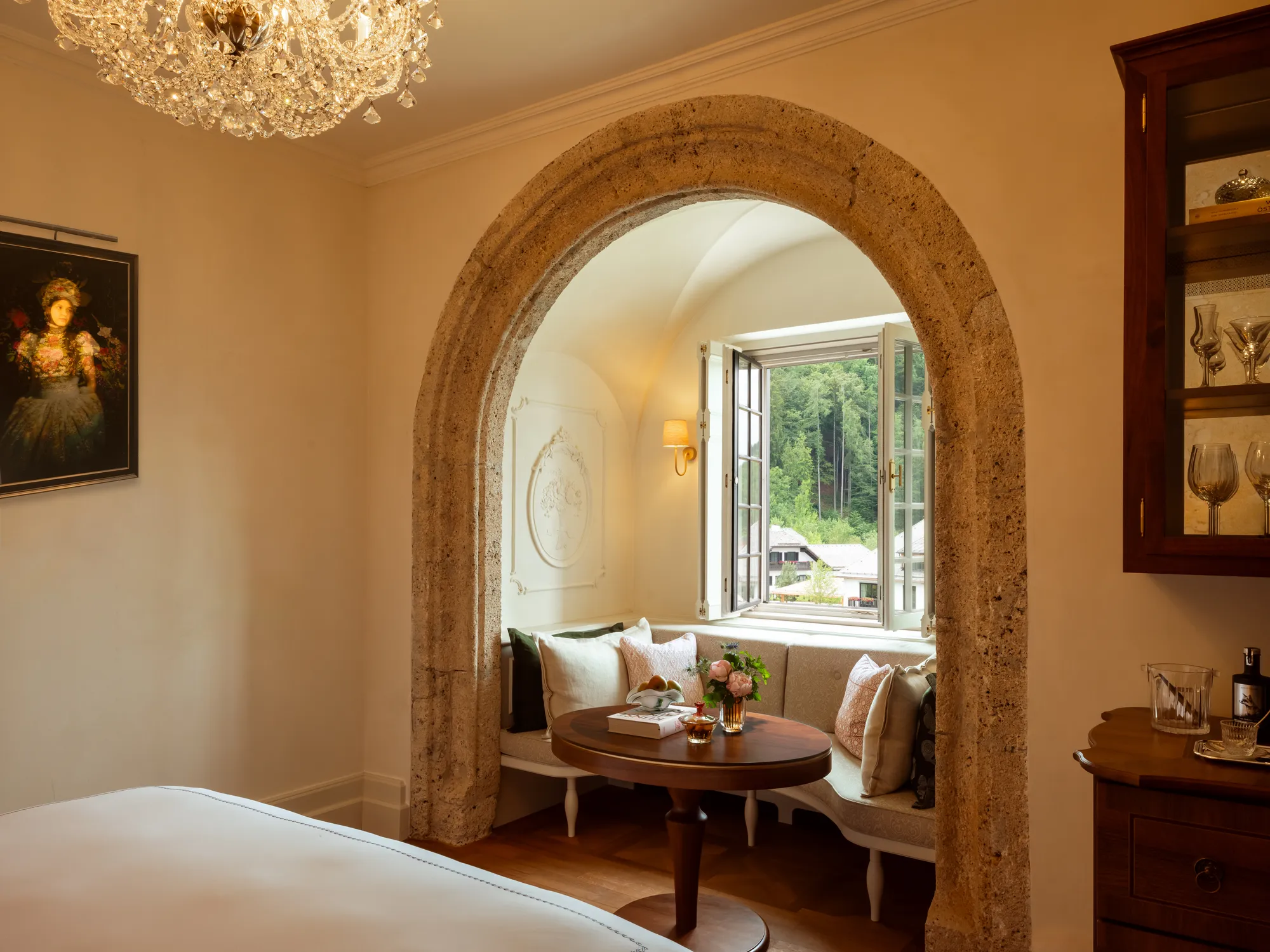 Heritage Room im Rosewood Schloss Fuschl: Fensternische hinter einem alten Steinbogen mit gepolsterter Bank und Blick ins Grüne