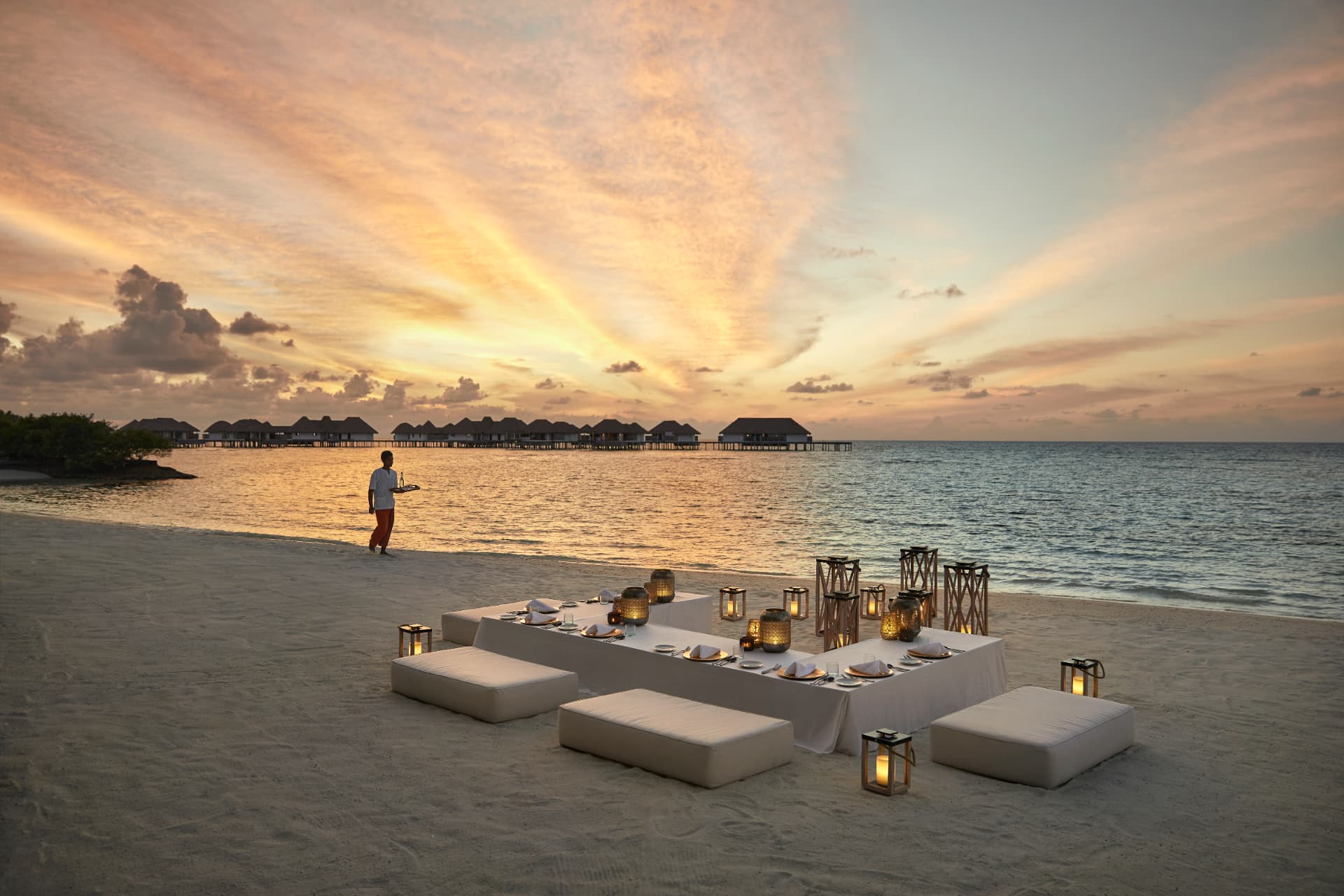 Lange Tafel am Strand mit Laternen und Blick auf die Wasservillen im Abendlicht