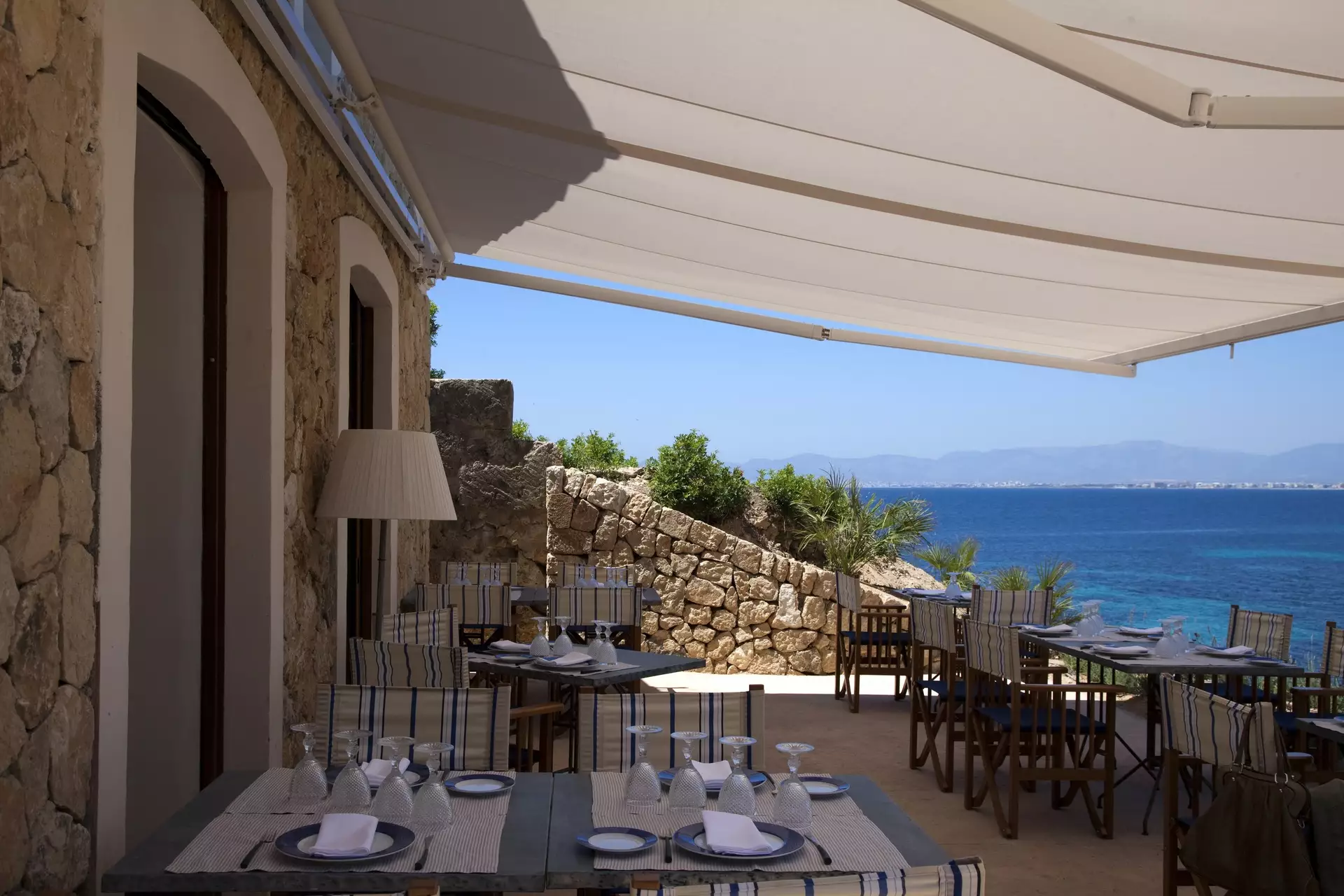 Restaurantterrasse unter hellem Segeldach mit Blick auf das türkise Meer