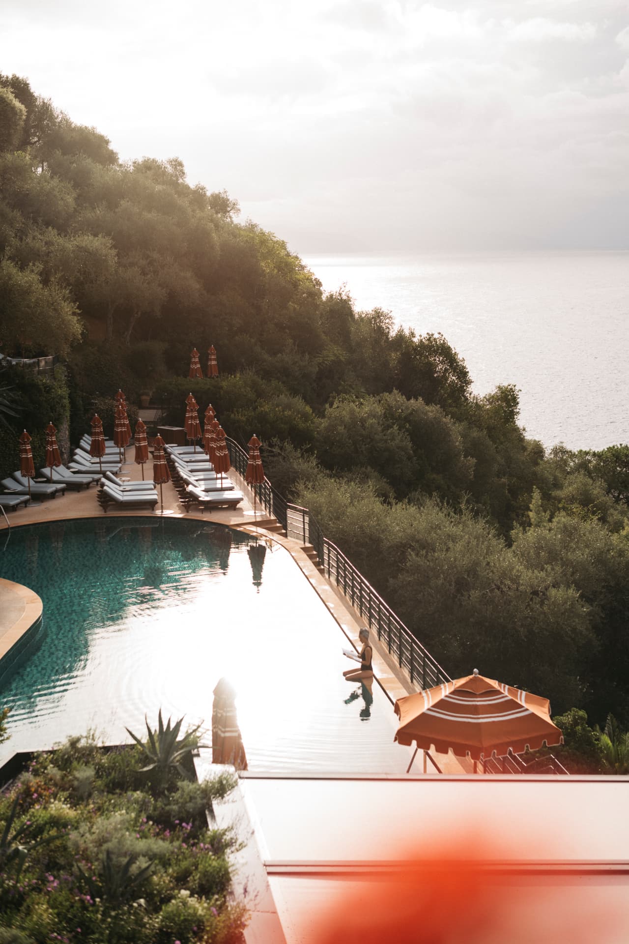 Der Pool mit Liegen und geschlossenen Schirmen im Gegenlicht des späten Nachmittags, dahinter das Ligurische Meer