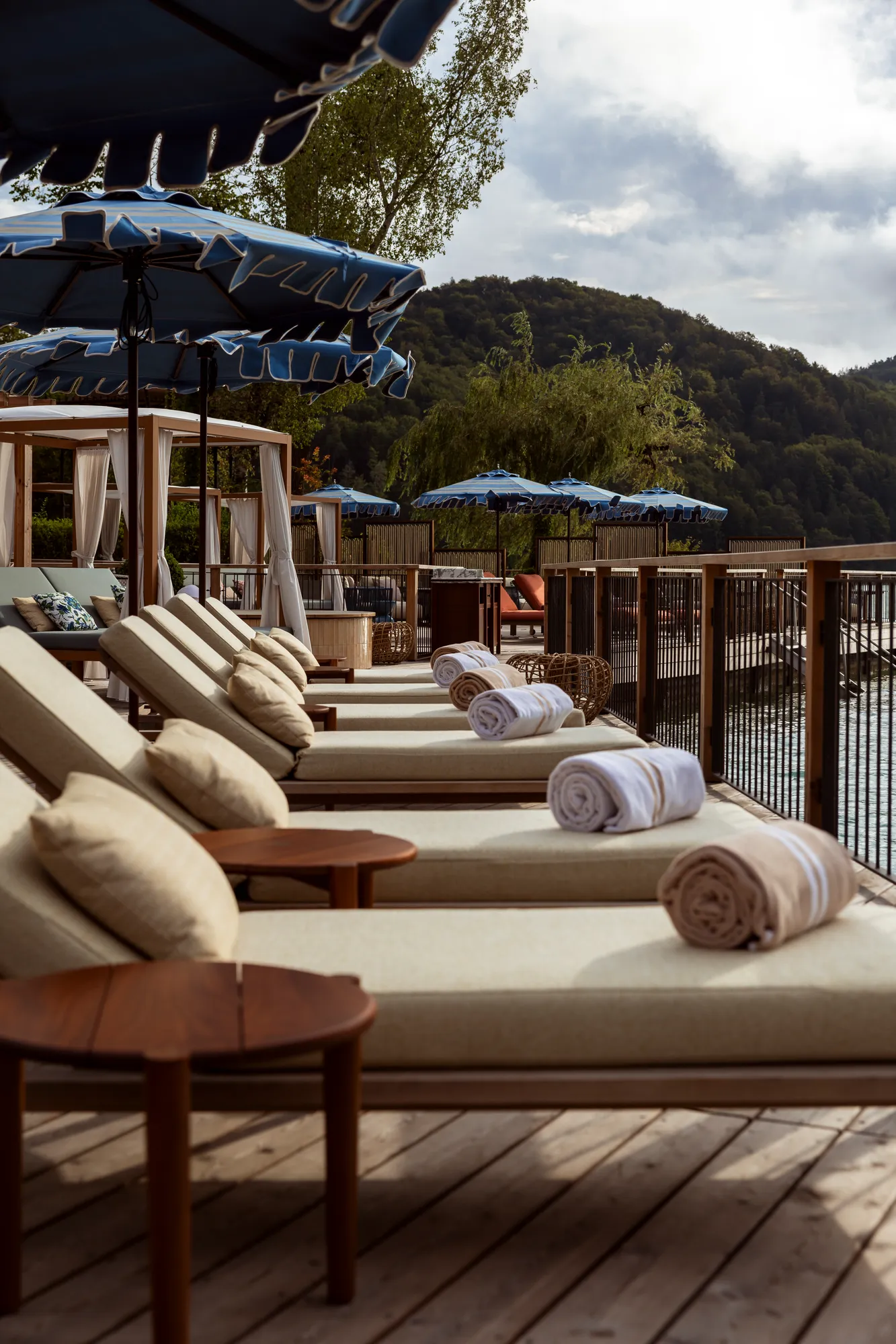 Liegen mit gerollten Handtüchern auf dem Holzdeck des See Clubs am Fuschlsee, dahinter bewaldete Hügel
