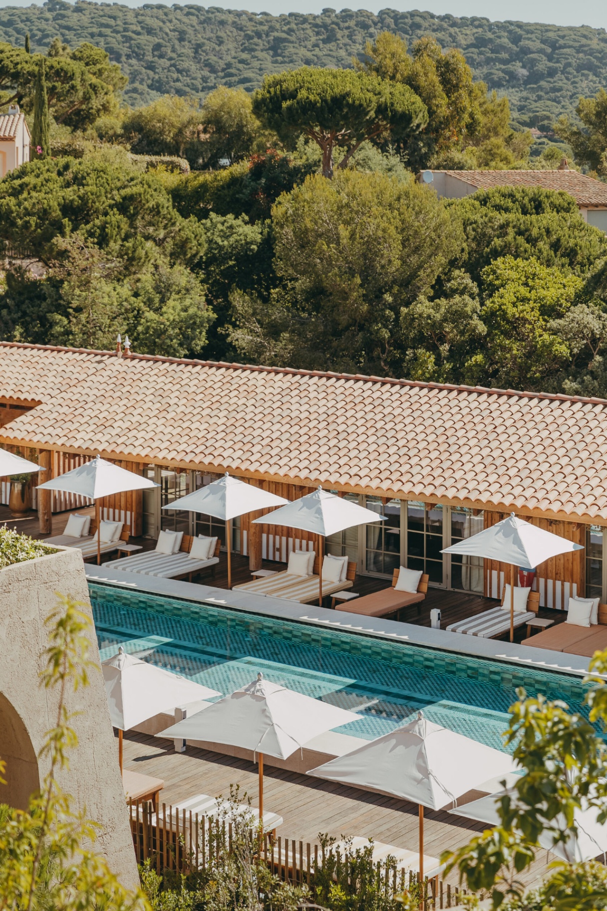 Langer Pool mit Cabanas und Sonnenschirmen vor bewaldeten Hügeln