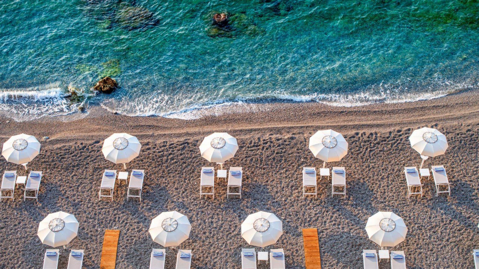 Kiesstrand des Borgo Santandrea mit weissen Sonnenschirmen aus der Vogelperspektive