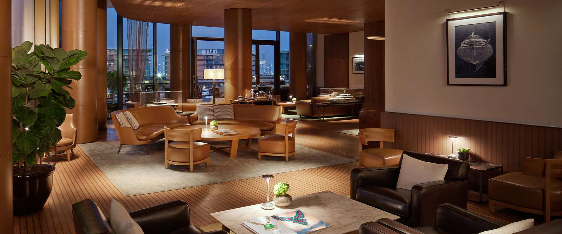 Lobby-Lounge am Abend mit Ledersofas, Nussbaumsäulen und Blick auf die Marina