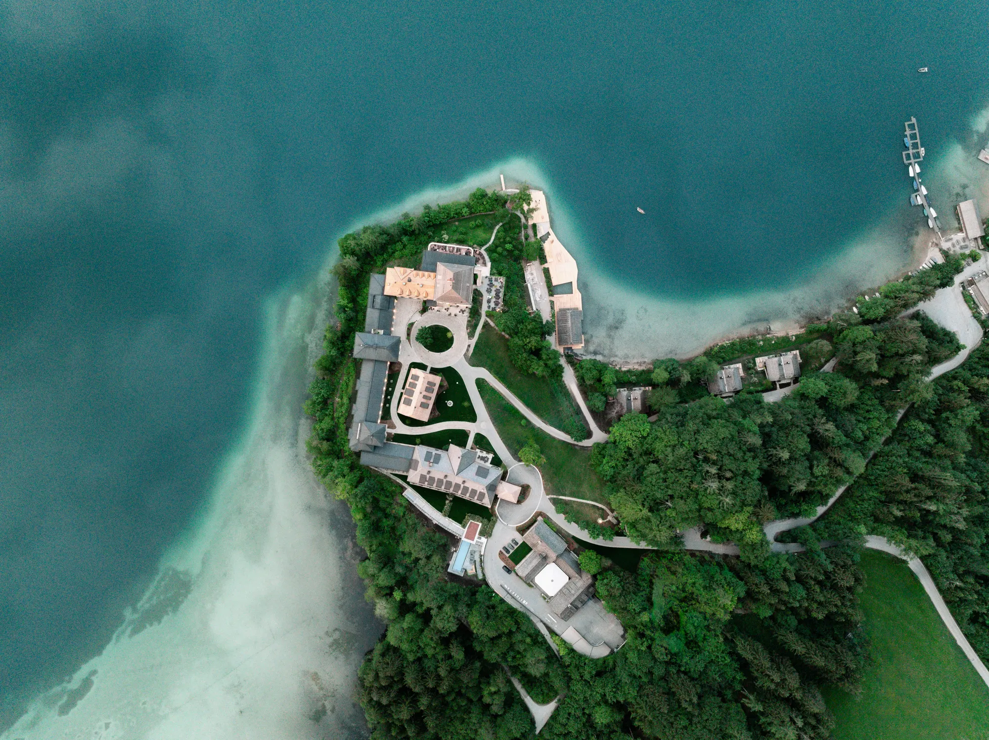 Senkrechte Luftaufnahme der bewaldeten Halbinsel mit dem Schloss Fuschl, umgeben vom türkisgrünen Fuschlsee