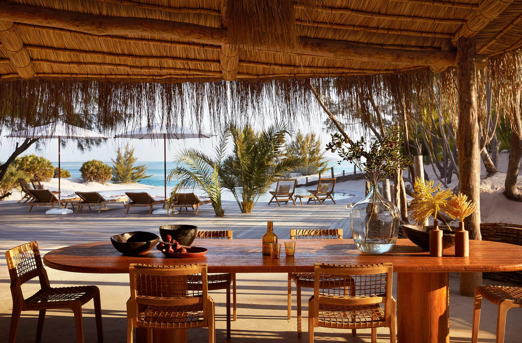 Esstisch unter dem Schilfdach mit Blick auf Pool, Palmen und Meer