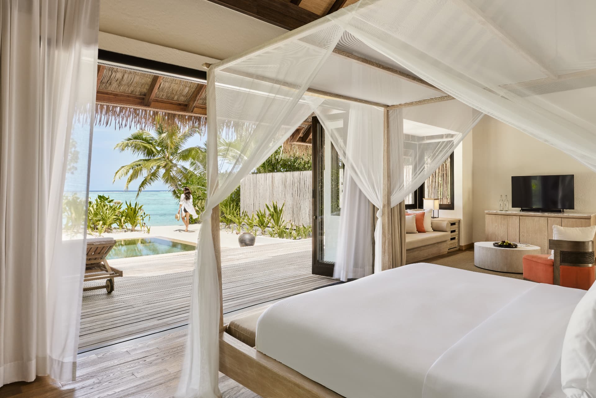 Schlafbereich der Beach Suite mit Moskitonetz und Blick auf Pool und Lagune