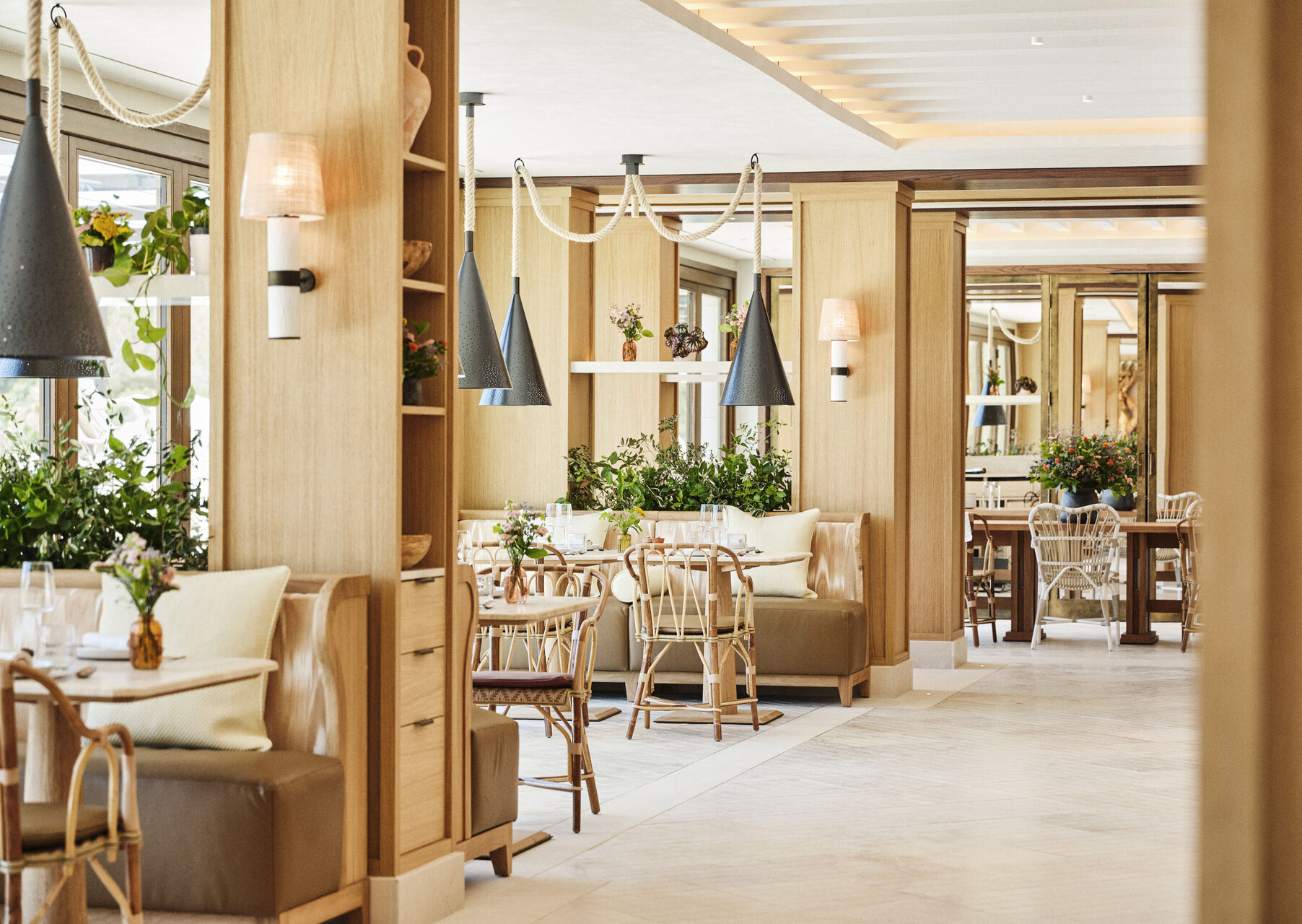 Restaurant in hellem Eichenholz mit Rattanstühlen, Bänken und viel Grün