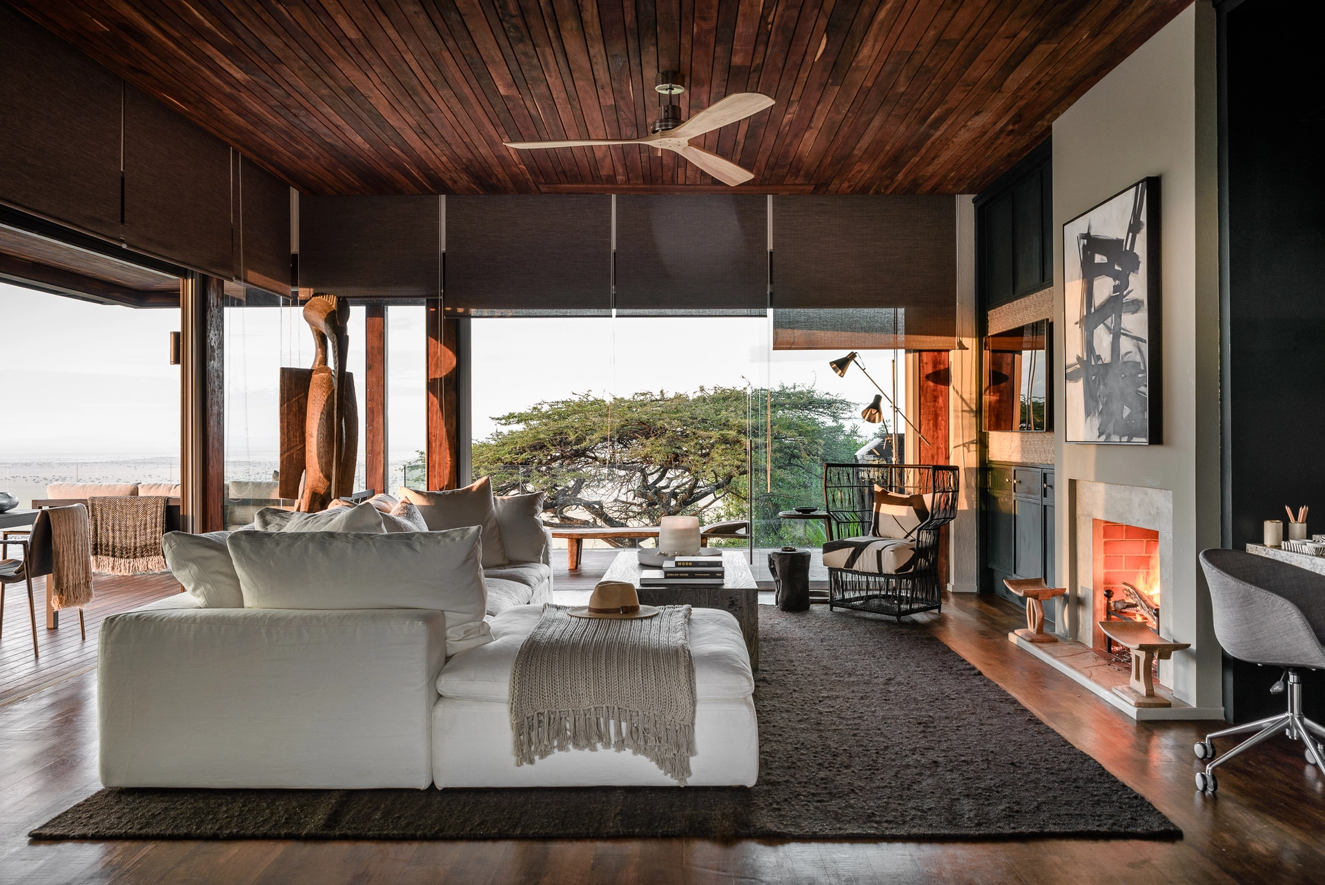 Wohnraum einer Villa der Sasakwa Lodge mit offenem Kamin und Blick auf eine Schirmakazie