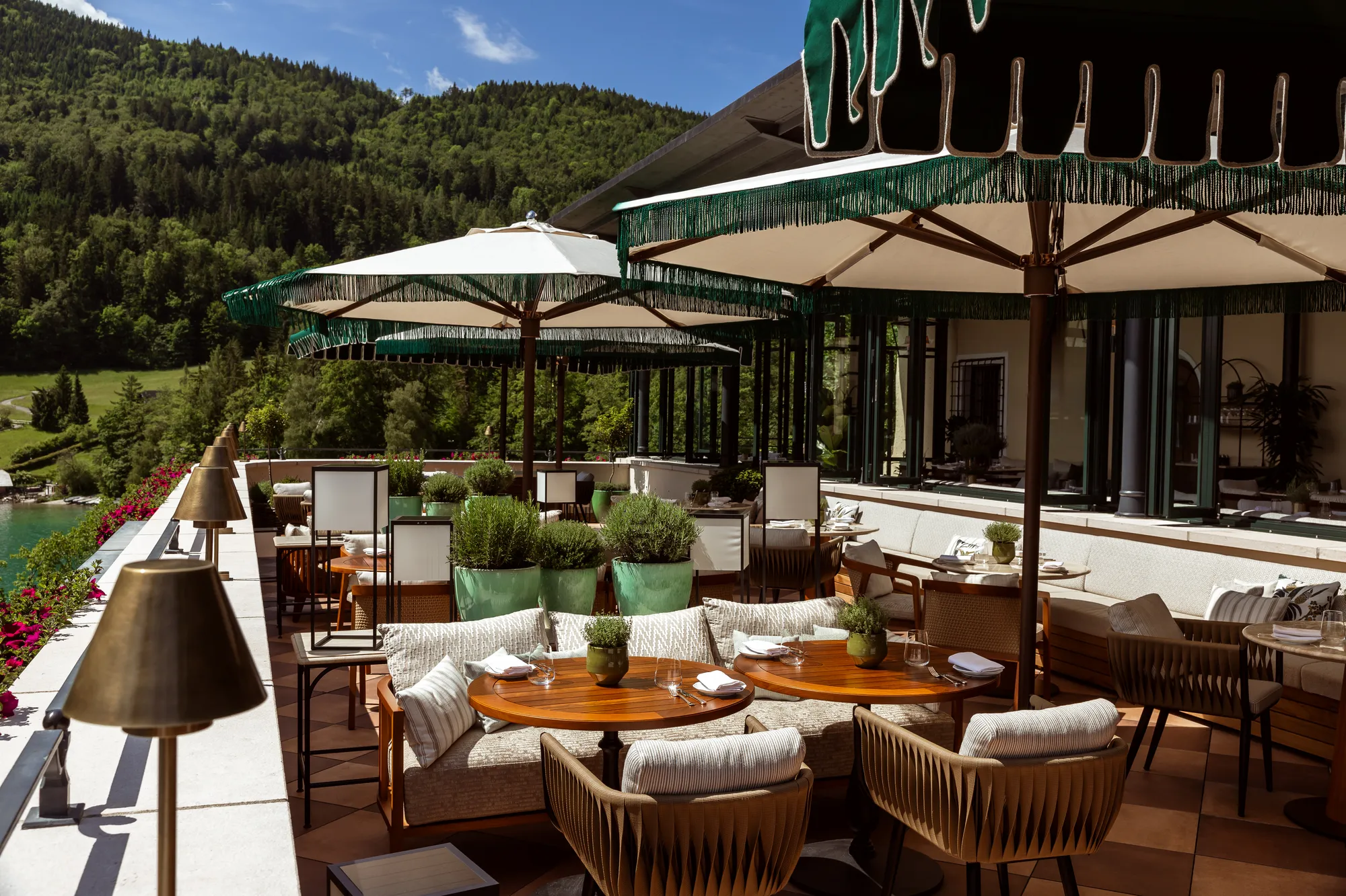 Die SeeTerrasse des Rosewood Schloss Fuschl mit Fransenschirmen, Holztischen und Blick über den Fuschlsee auf bewaldete Hänge