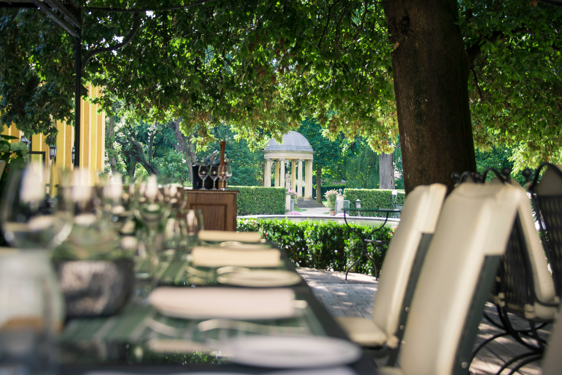 Gedeckte Tafel unter alten Bäumen mit Blick auf den Tempietto im Garten