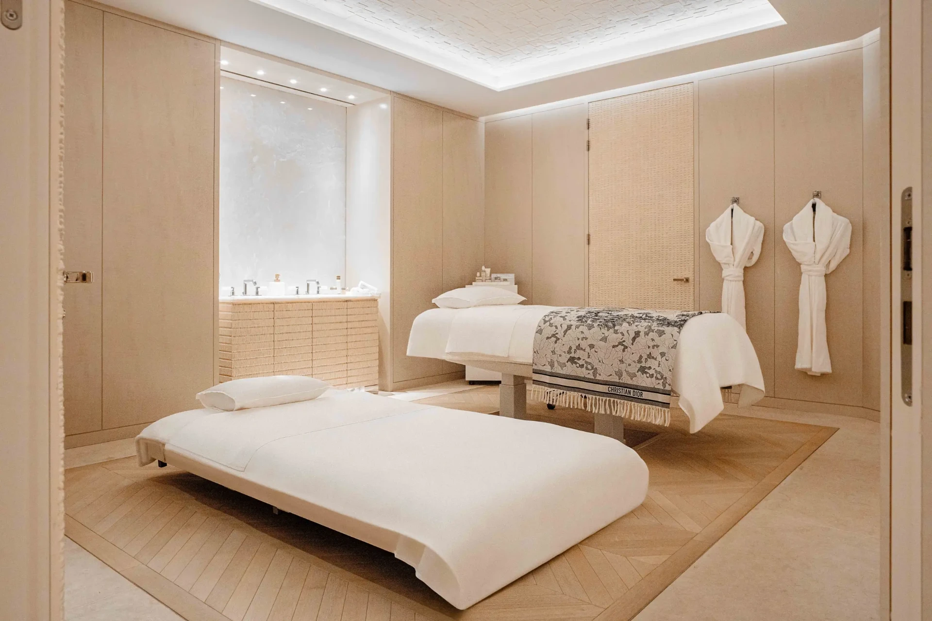 Behandlungsraum des Dior Spa mit zwei Liegen, hellem Holz und Fischgrätparkett