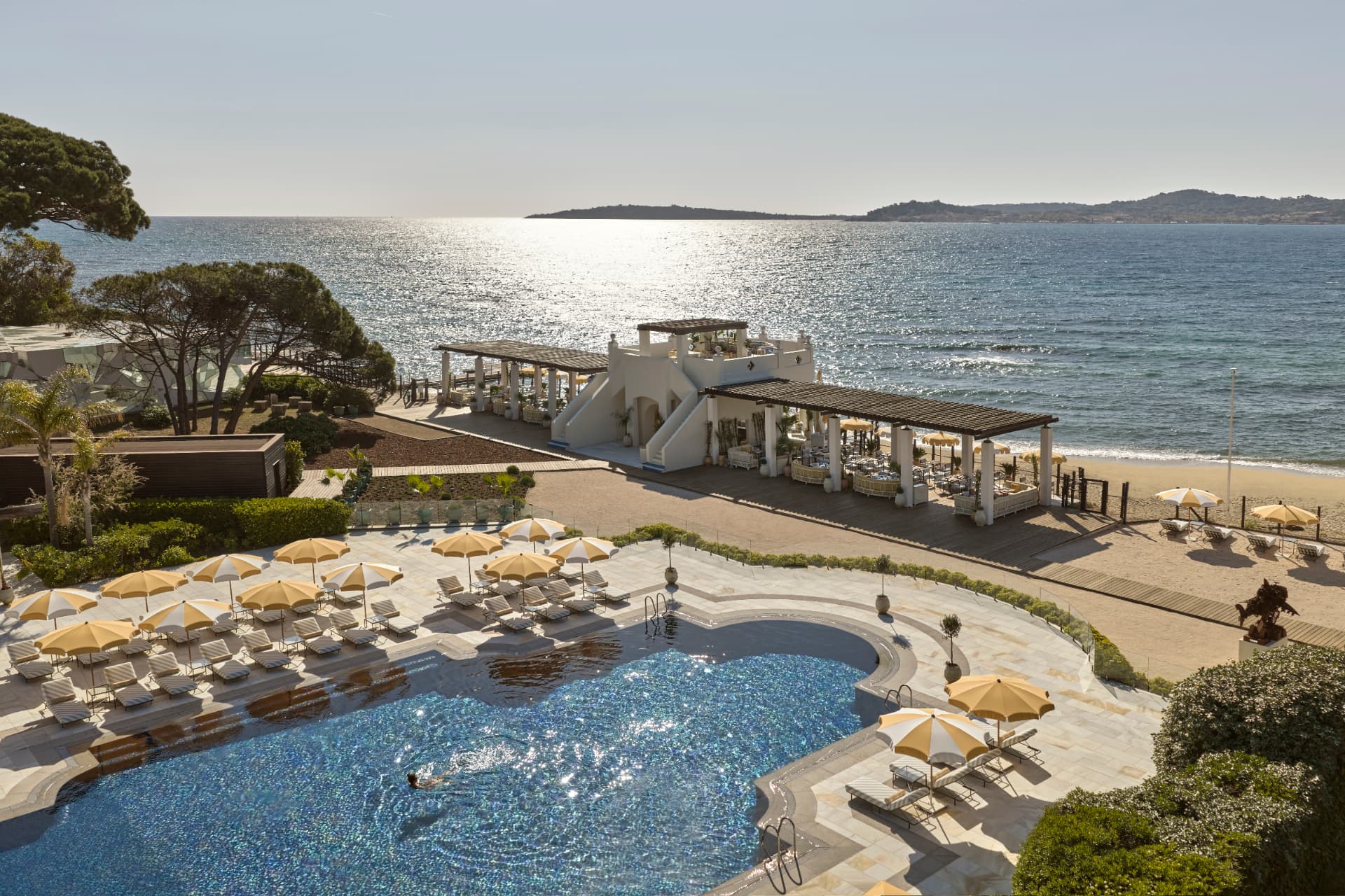 Pool mit gelben Schirmen, dahinter der Strandclub und der Golf von Saint-Tropez