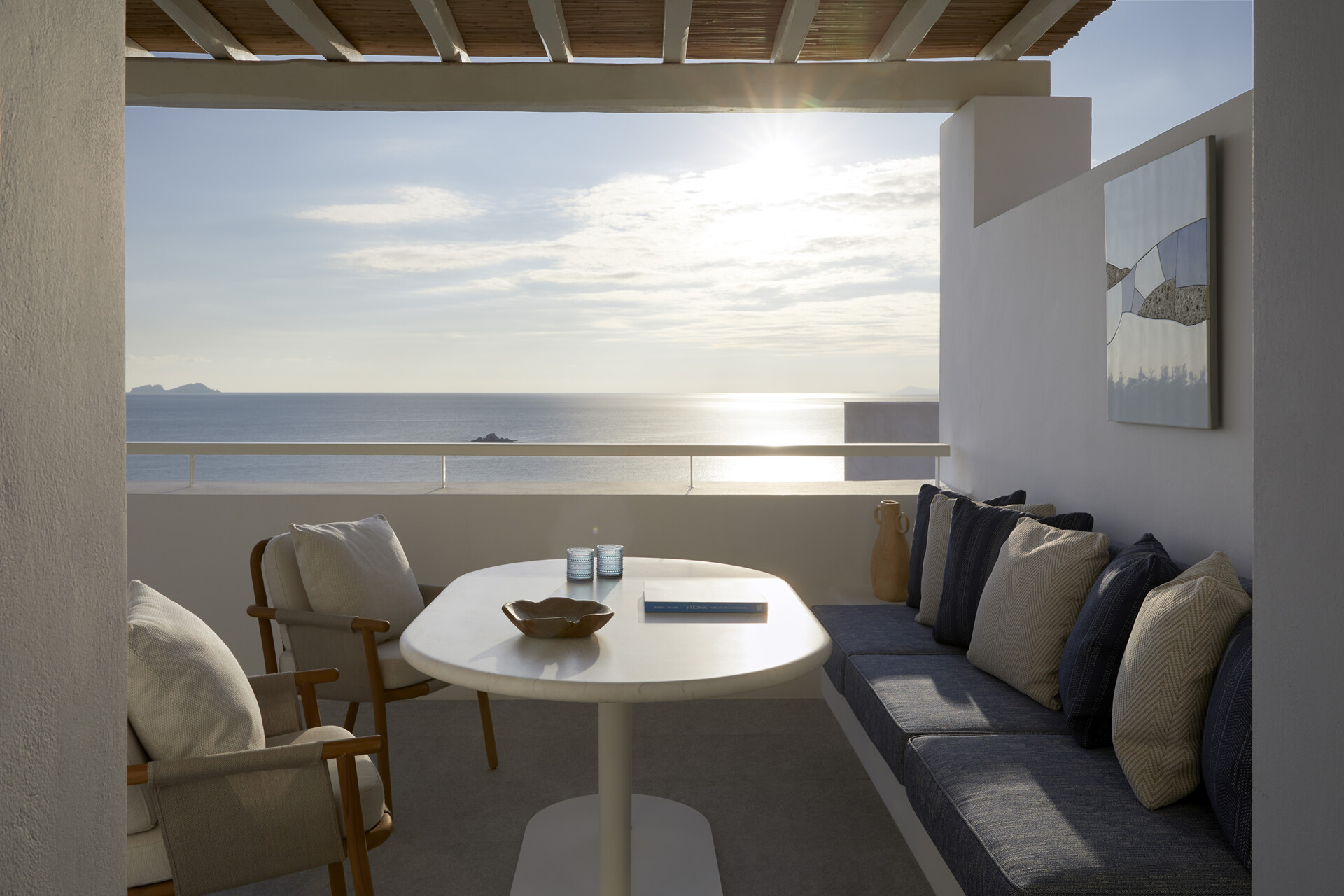Gedeckter Tisch unter der Pergola mit Bank, Kissen und Sonnenuntergang über der Ägäis