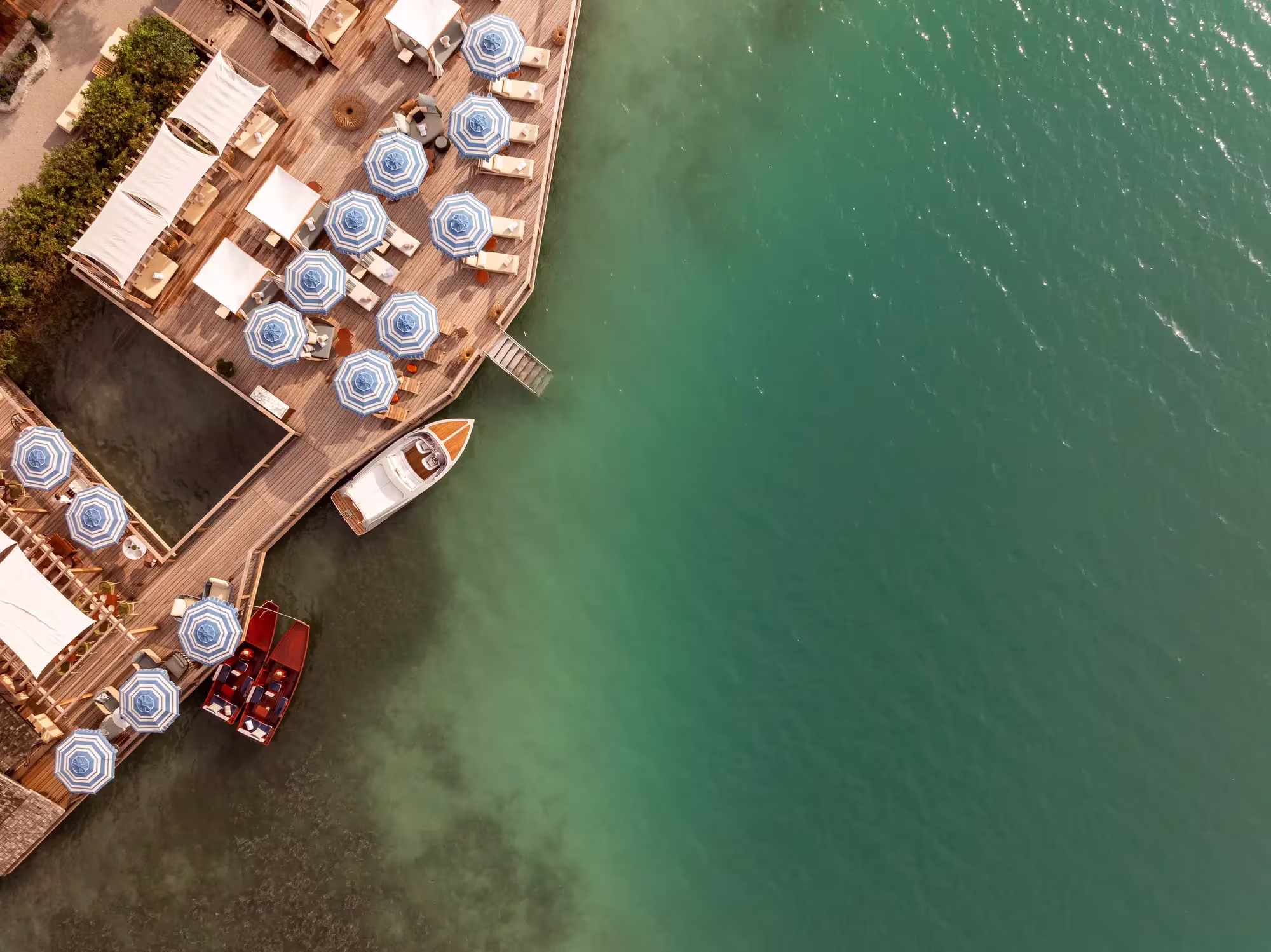 Der See Club des Rosewood Schloss Fuschl direkt am Wasser mit Stegen, Sonnenschirmen und Blick über den Fuschlsee