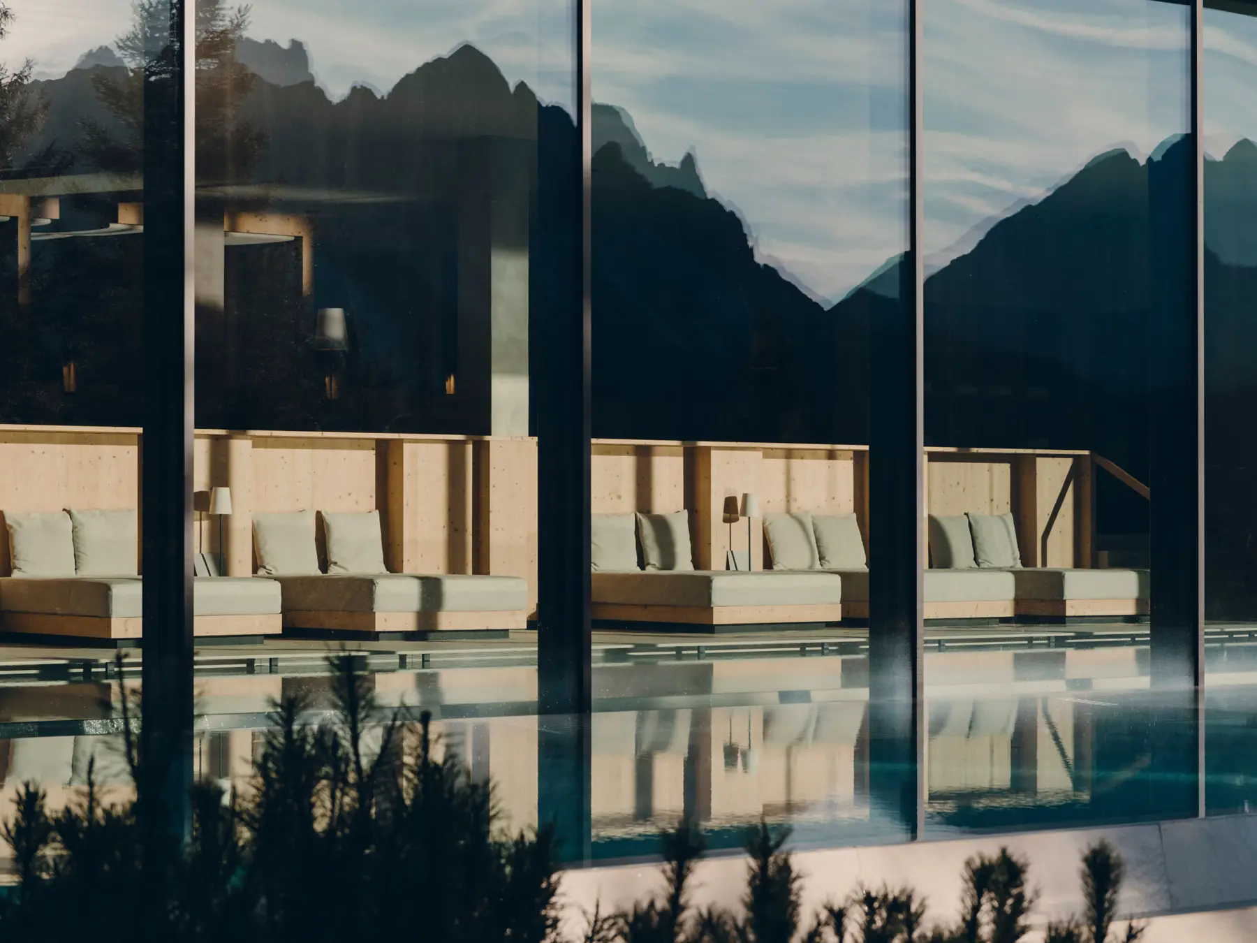 Poolhaus hinter grossen Fenstern, in denen sich die Dolomiten spiegeln