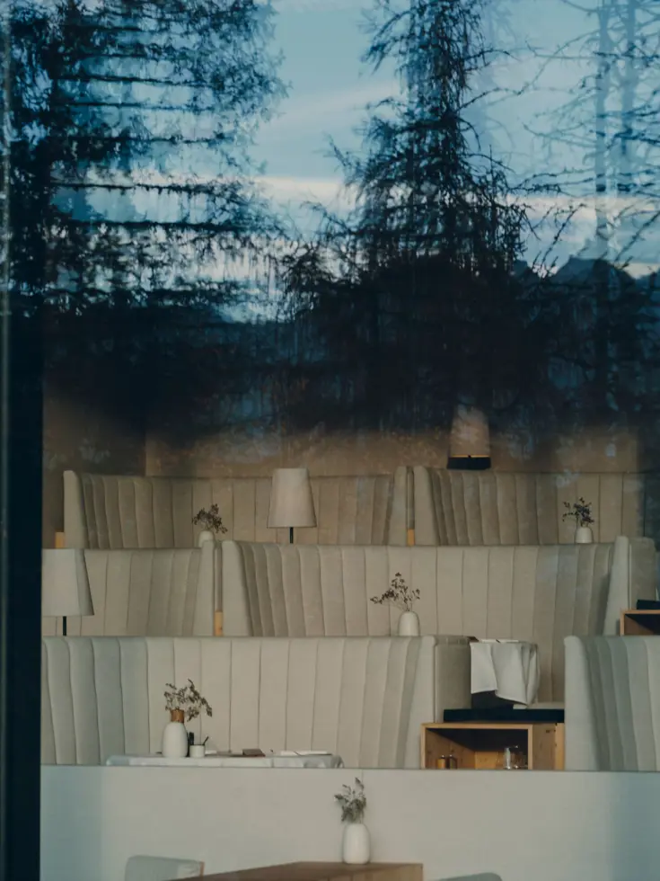 Restaurant hinter Glas, helle Polsterbänke und Lärchen, die sich in der Scheibe spiegeln