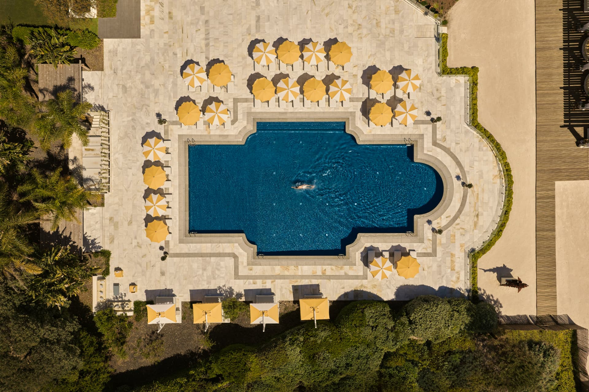 Der Pool von oben, umgeben von gelb-weißen Schirmen auf hellem Stein