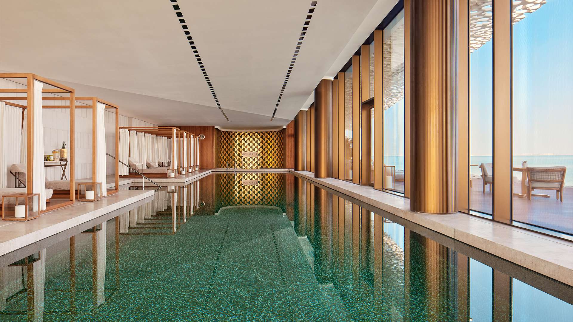 Langer Innenpool des Spa mit grünem Mosaik und Fensterfront zum Meer