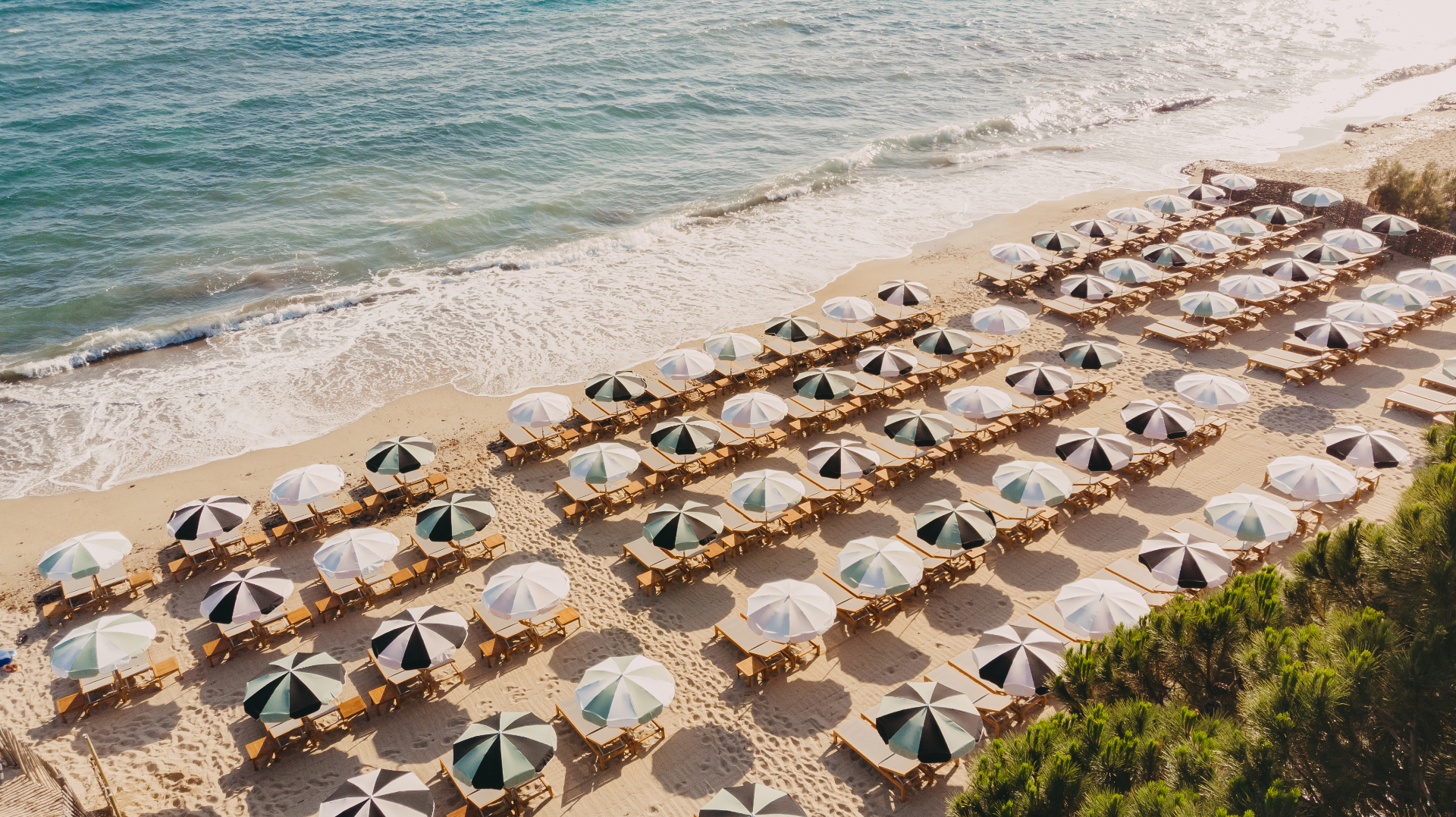 Sonnenschirme und Liegen am Sandstrand von Gigaro aus der Luft